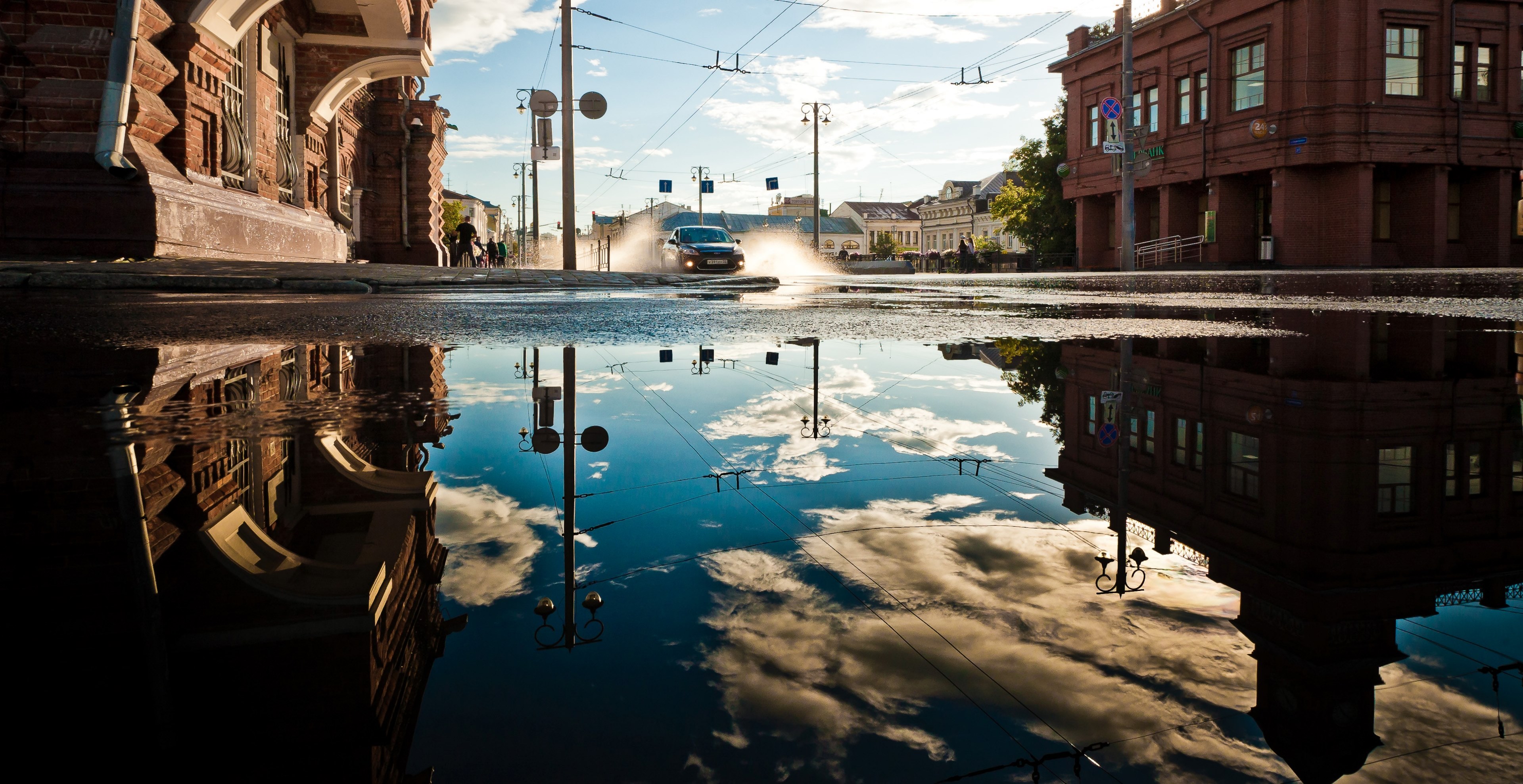 black car driving through puddle reflecting the sky and buildings on a street in vladimir, black car puddle vladimir 4k, HD Wallpaper
