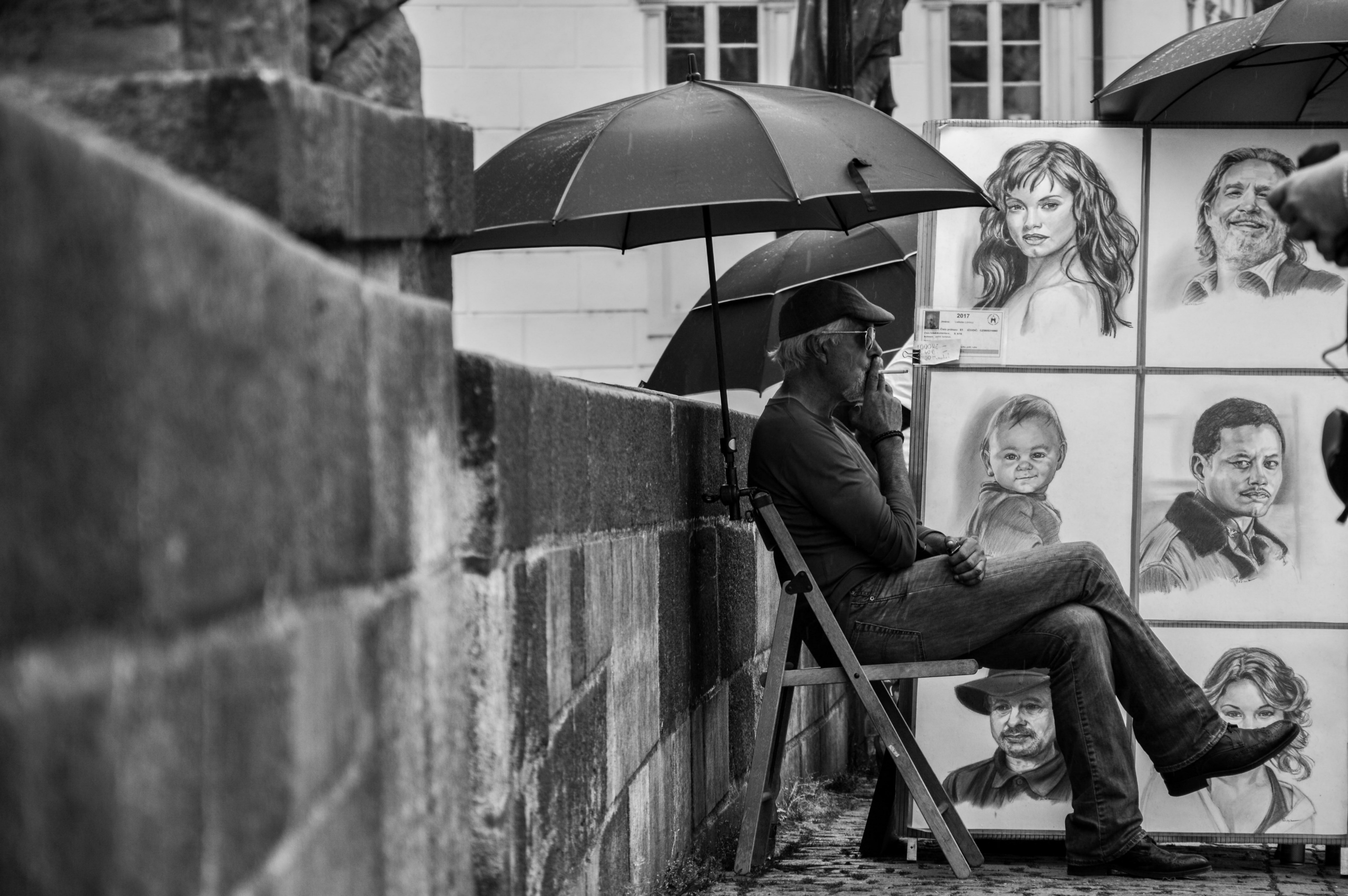 black and white photo of man smoking under umbrella next to hand drawings in prague, prague story 4k, HD Wallpaper