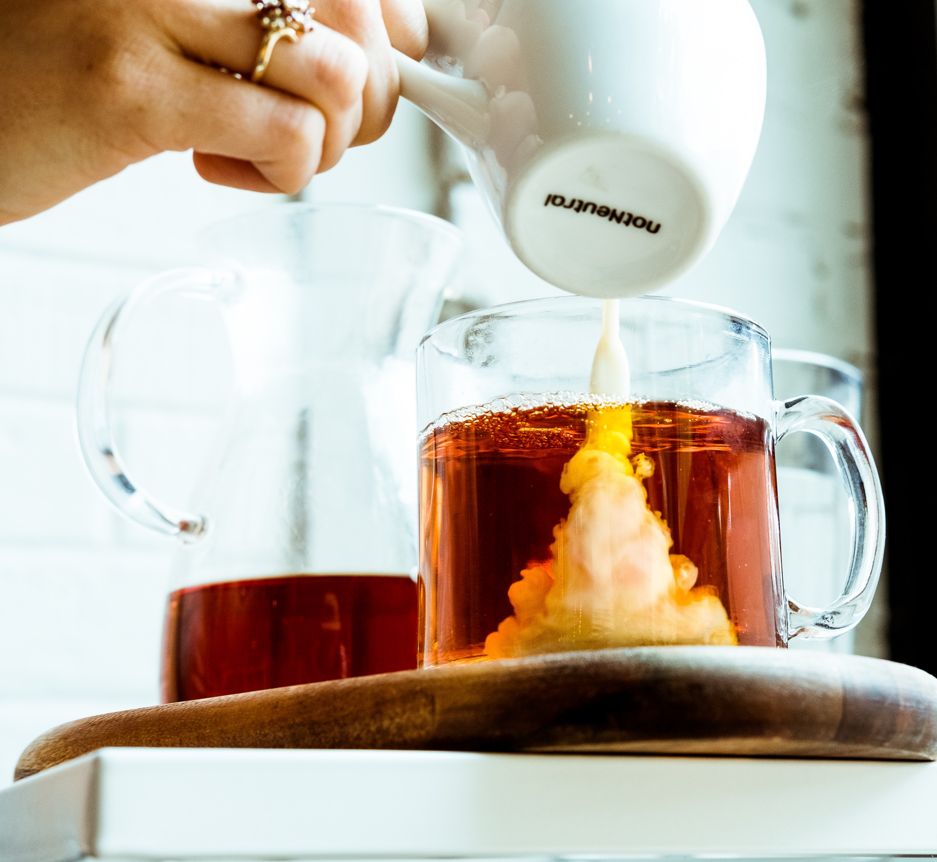 a person pouring milk over a glass mug of tea beside a glass jug of tea, milk pouring over tea 4k, HD Wallpaper