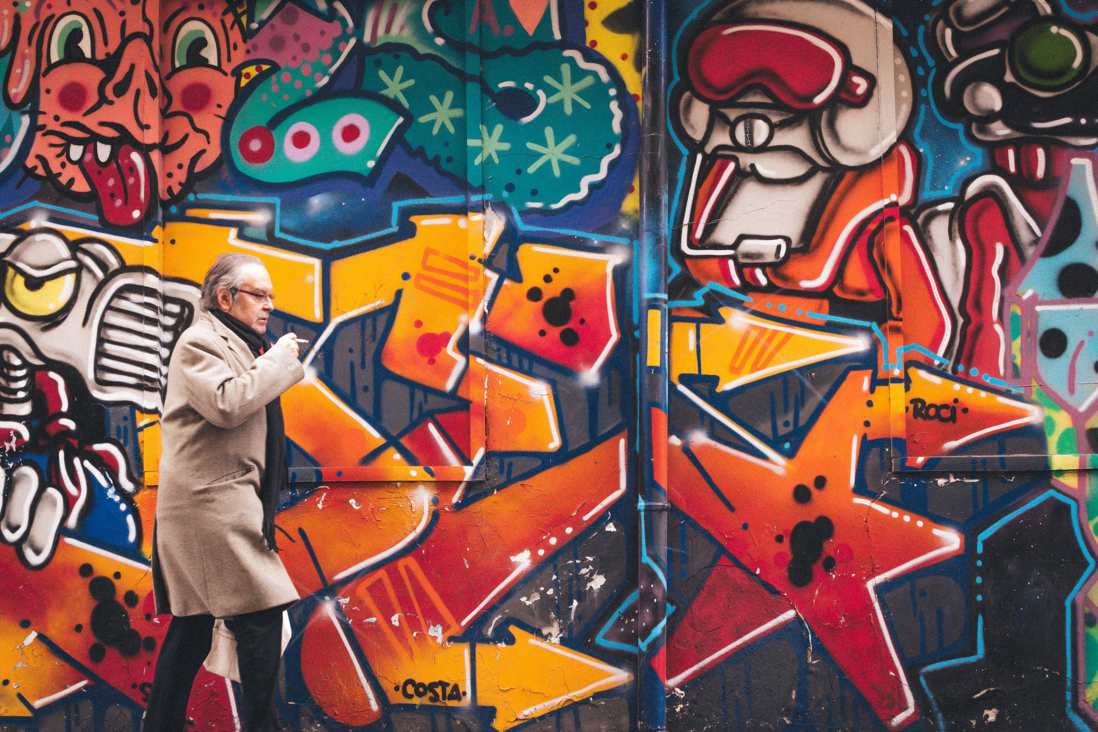 older man in long beige trench coat smoking near colorful street art graffiti mural, man smoking in front of graffiti 4k, HD Wallpaper