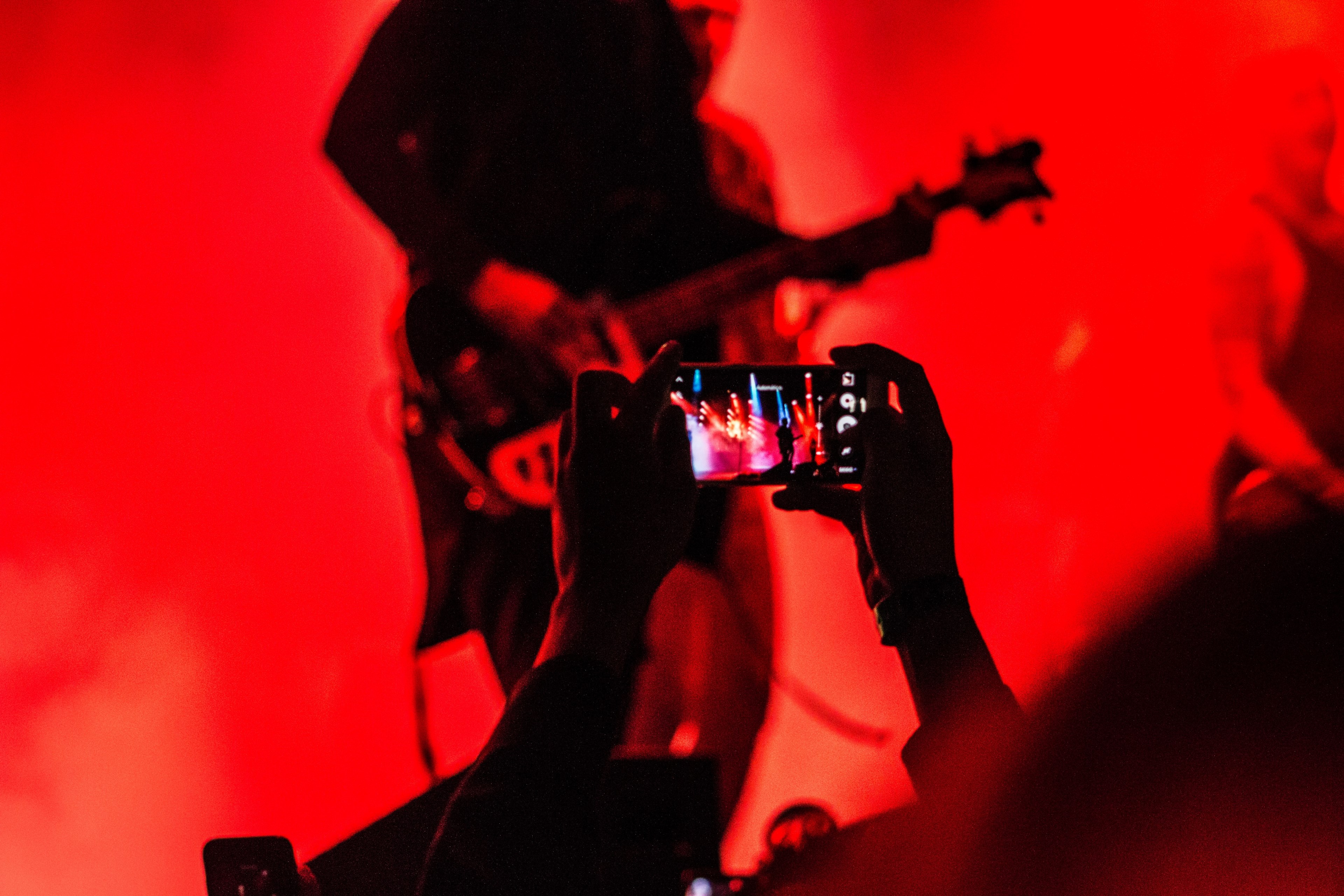 a guitarist performs on stage in red light while an audience member records a concert on their phone, guitarist bathed in red light 4k, HD Wallpaper