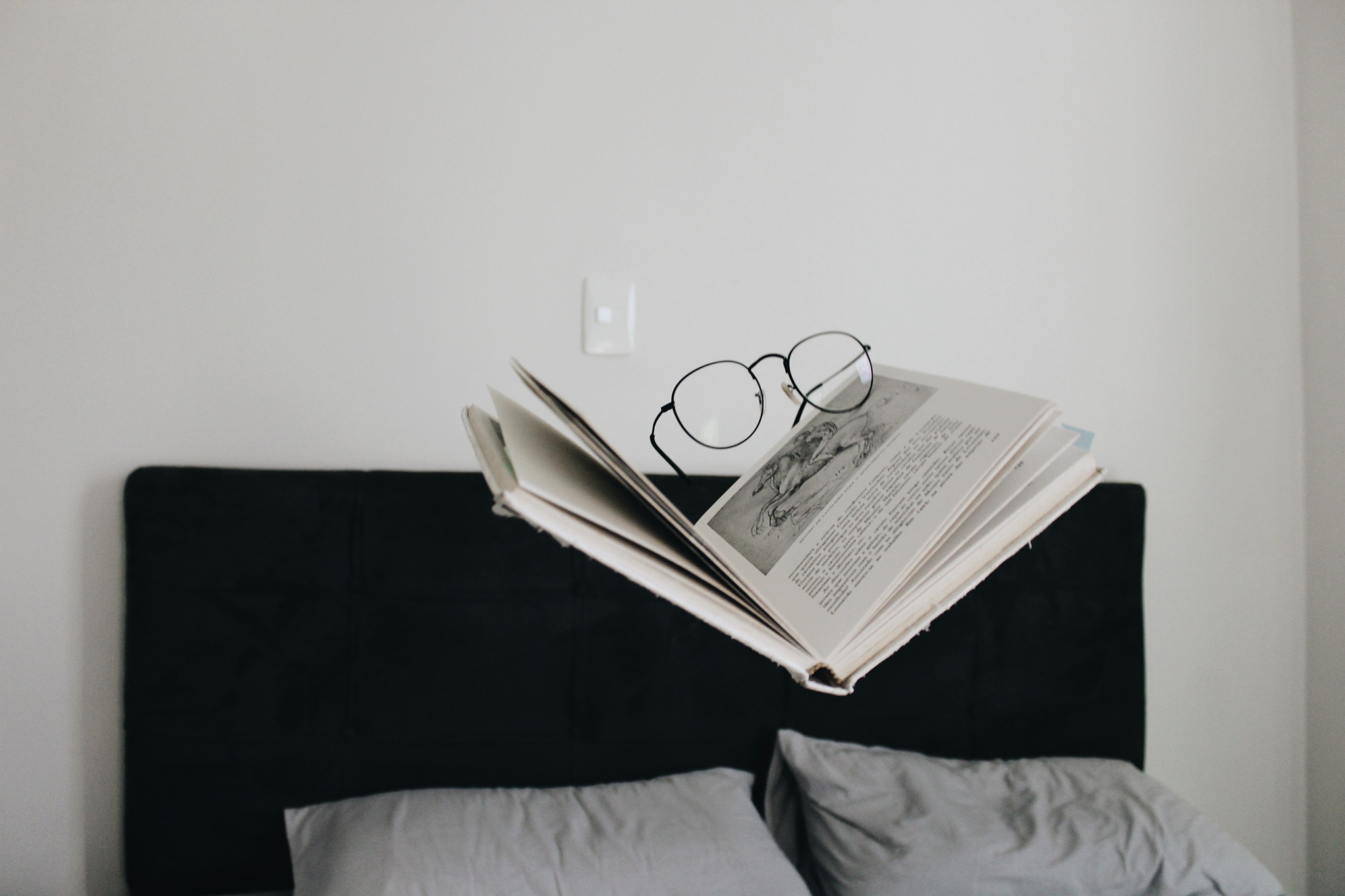 a pair of glaases on a partially opened book floating above a black and gray bed, glasses and book 4k, HD Wallpaper