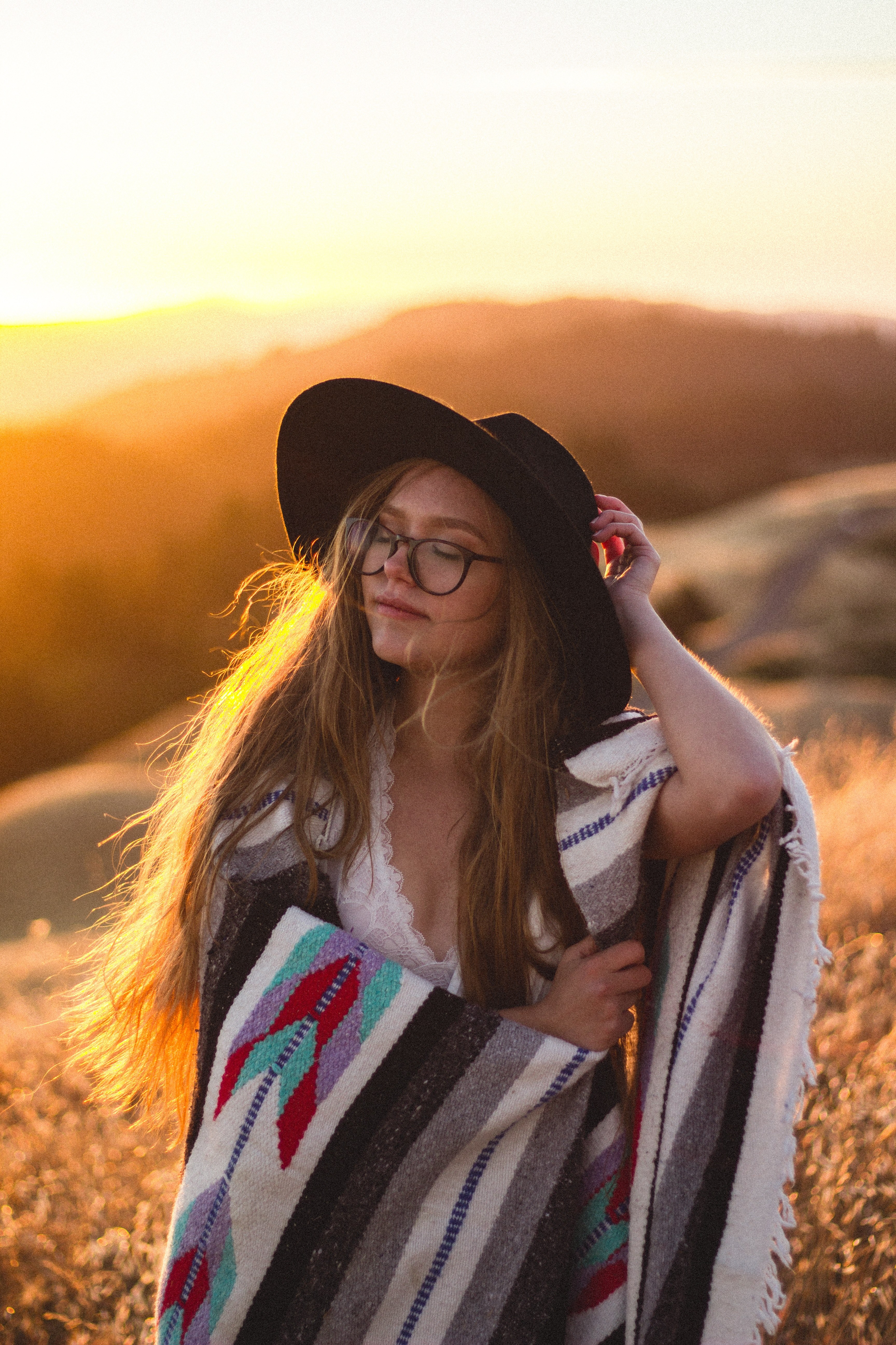 a woman wearing a hat and glasses is wrapped in a tribal blanket in mount tamalpais state park at golden hour, young woman at mount tamalpais state park 4k, Phone HD Wallpaper