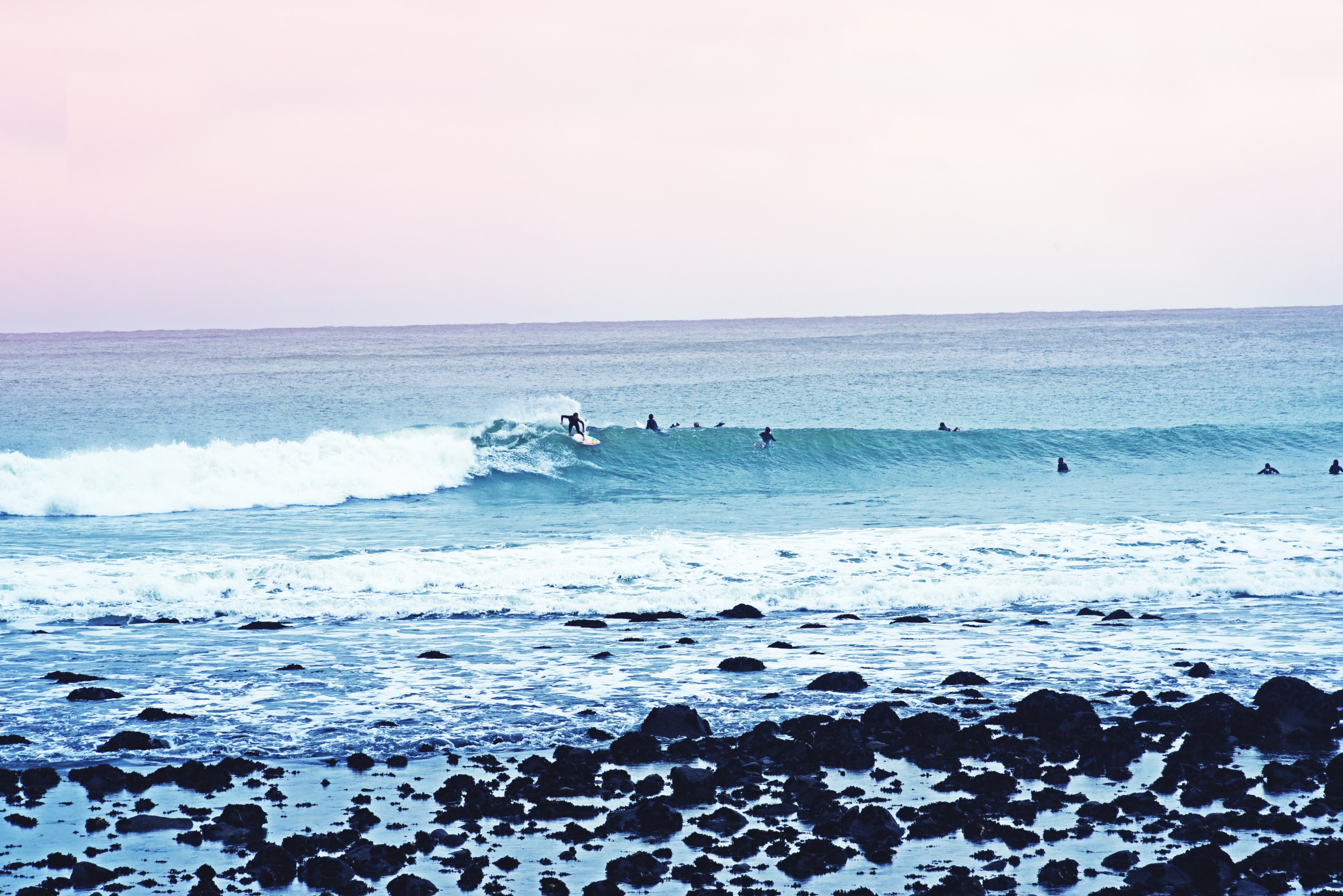 a pale shot of a surfer riding a wave with silhouettes of other people swimming in the sea nearby, braving the wave 4k, HD Wallpaper