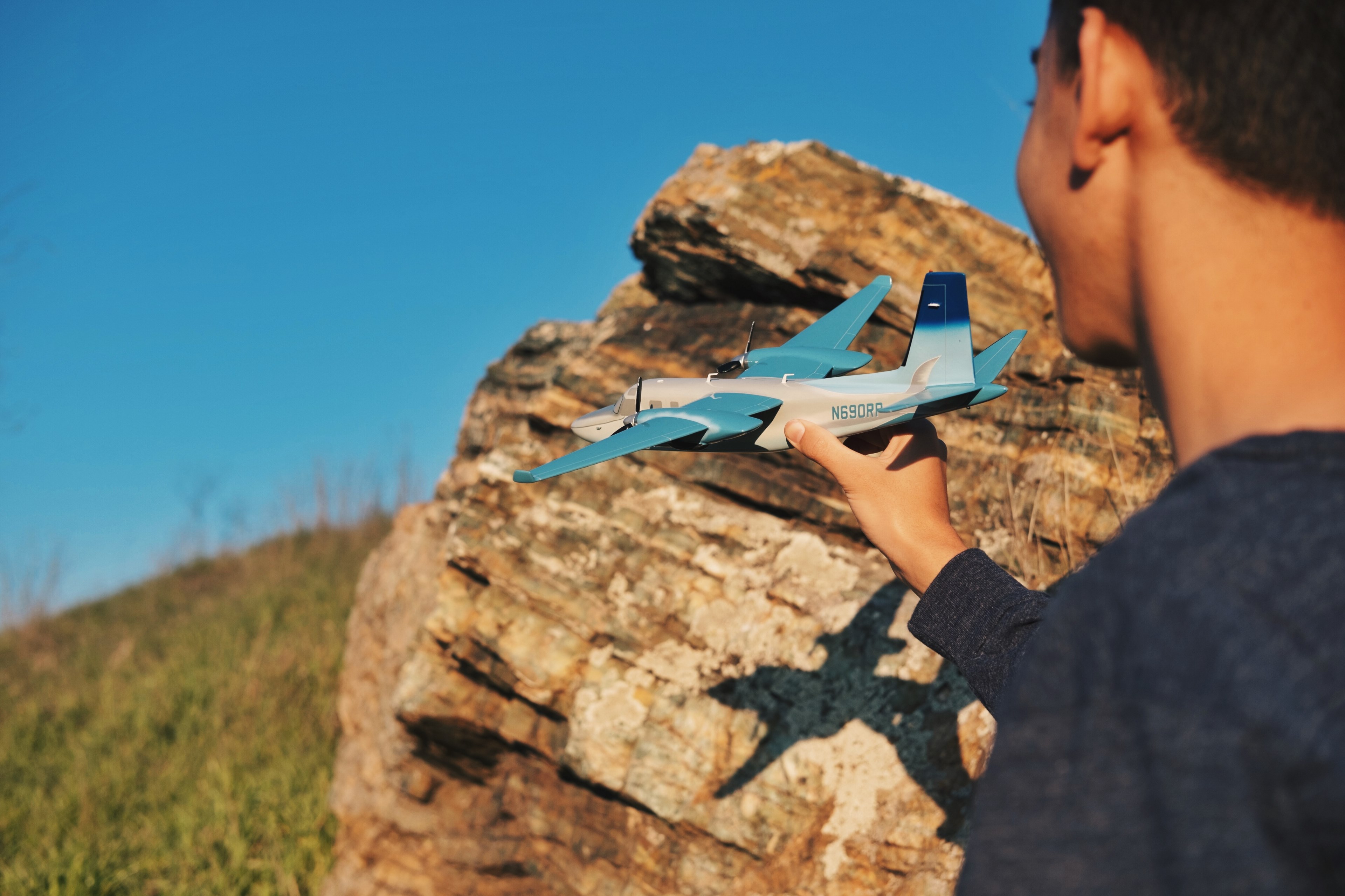 a boy holds a model airplane casting a shadow on a rock before a blue sky, shadow of a model airplane 4k, HD Wallpaper