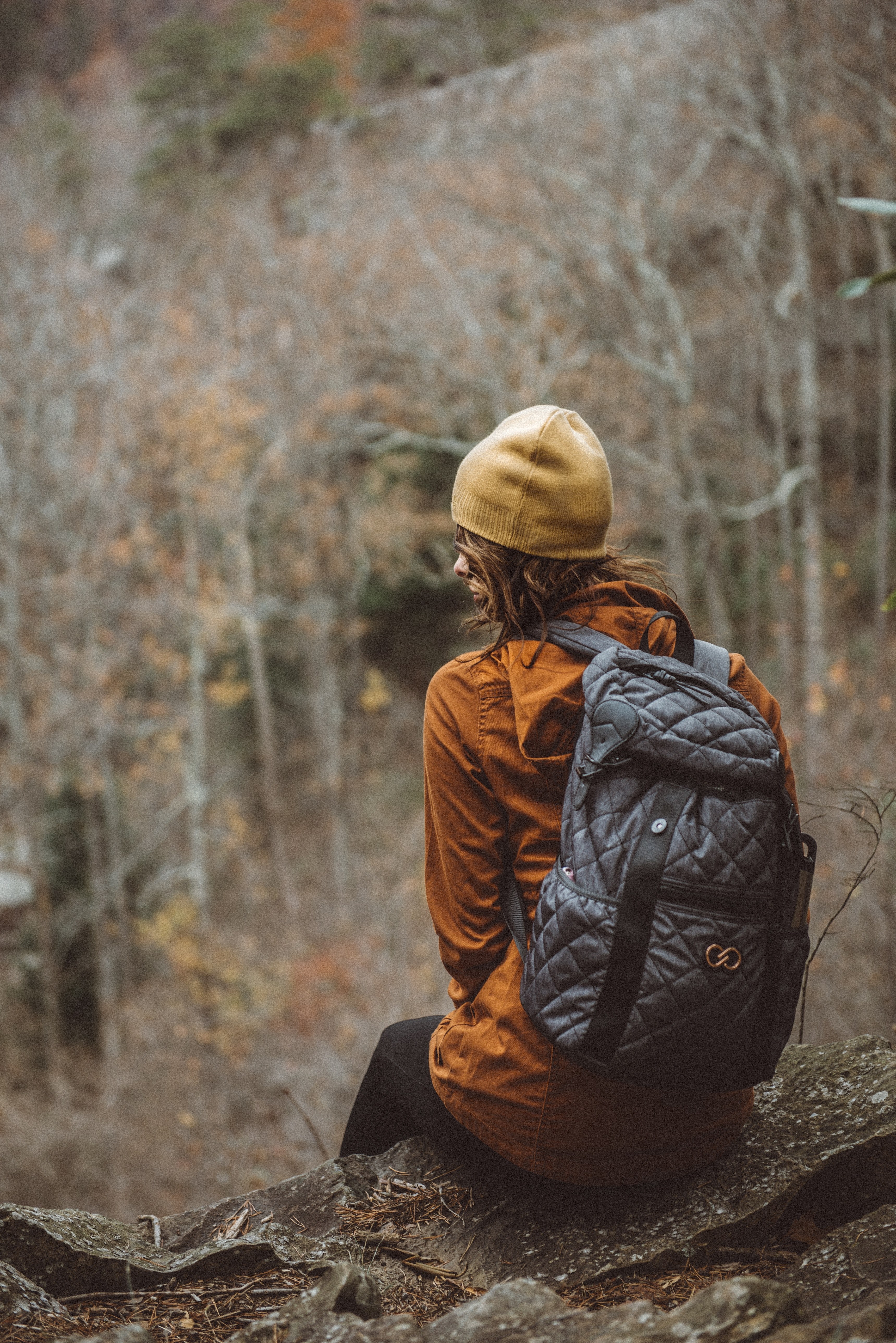 a person sitting on a ledge wearing a backpack hat and a jacket, person on ledge 4k, Phone HD Wallpaper