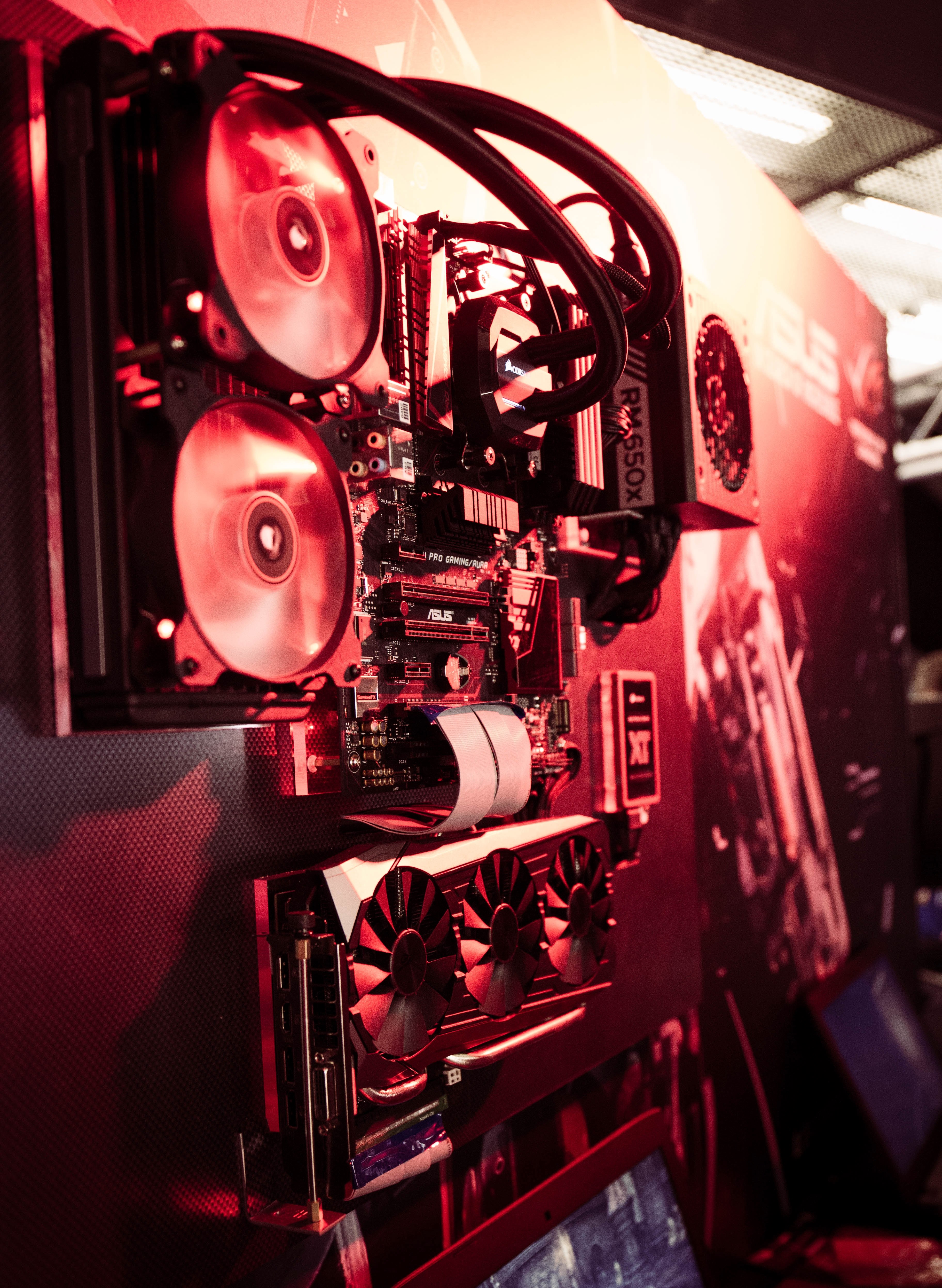a computer without the case showing the motherboard cooling fans graphics cards and power supply mounted on a red lit wall labeled asus in a gaming convention, gaming pc 4k, Phone HD Wallpaper