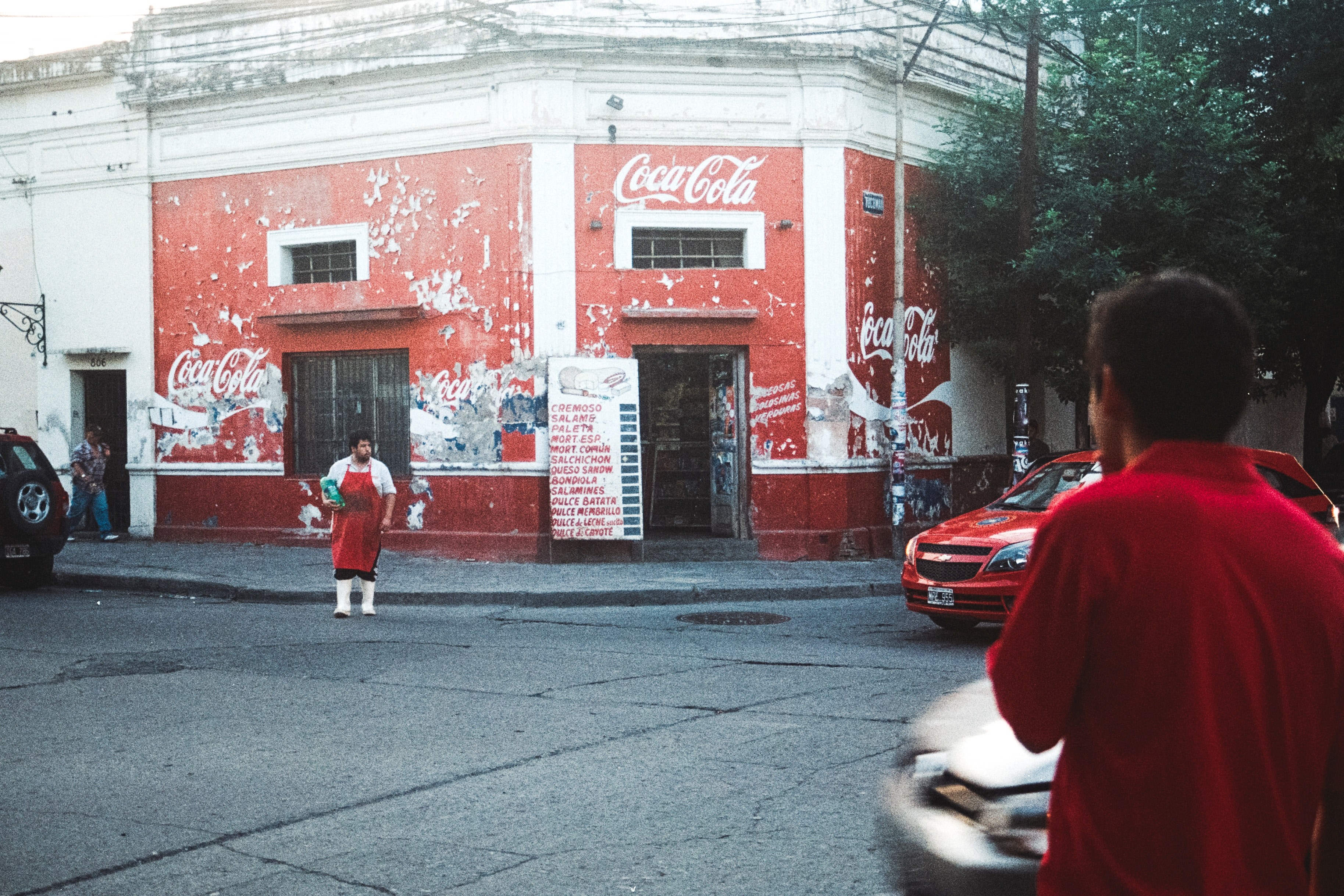a person in a red apron crosses the street outside a red shop with coca cola logos, chop with coca cola logos 4k, HD Wallpaper