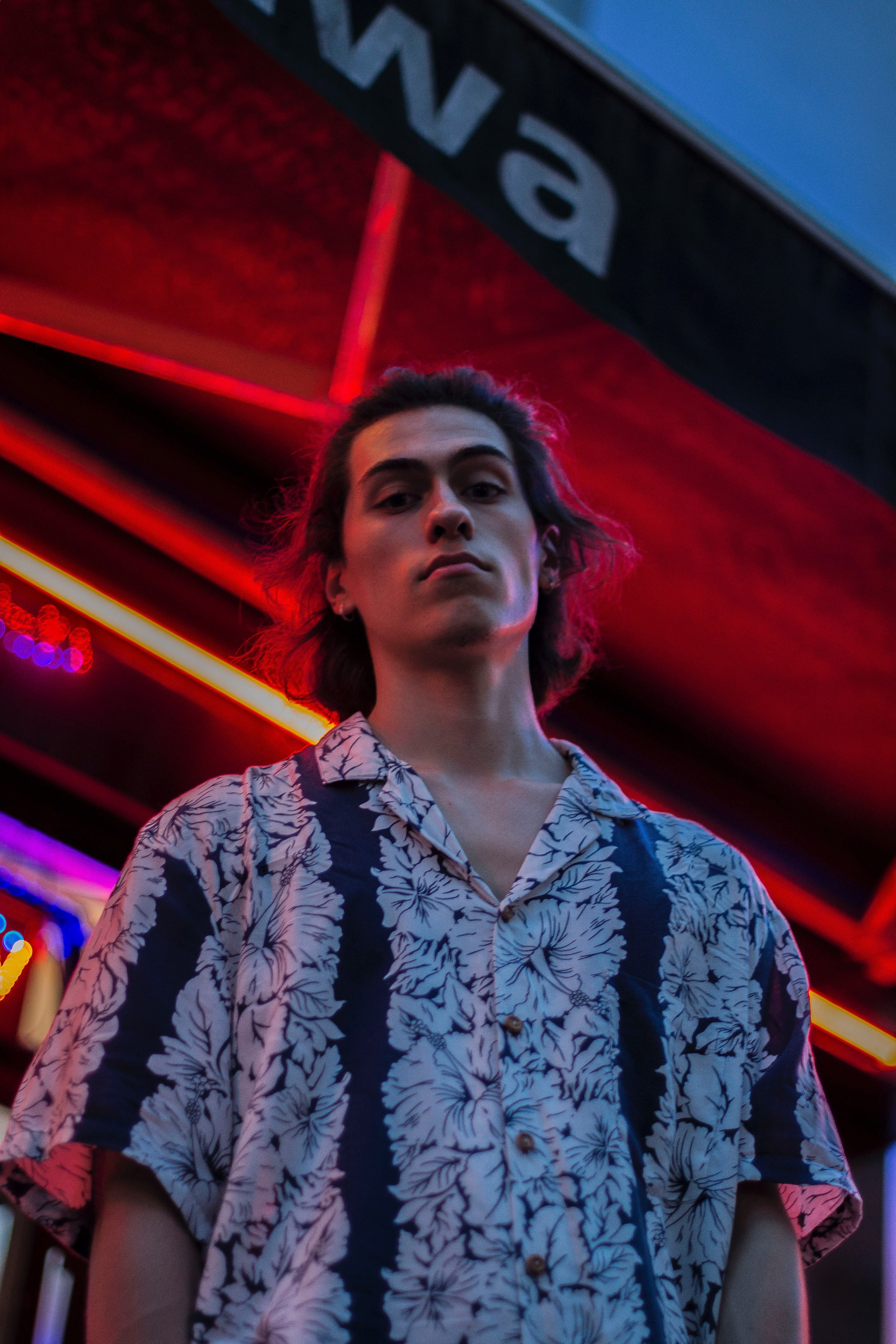 a man in a floral shirt stands in front of a neon building facade in paris, man in front of neon building 4k, Phone HD Wallpaper