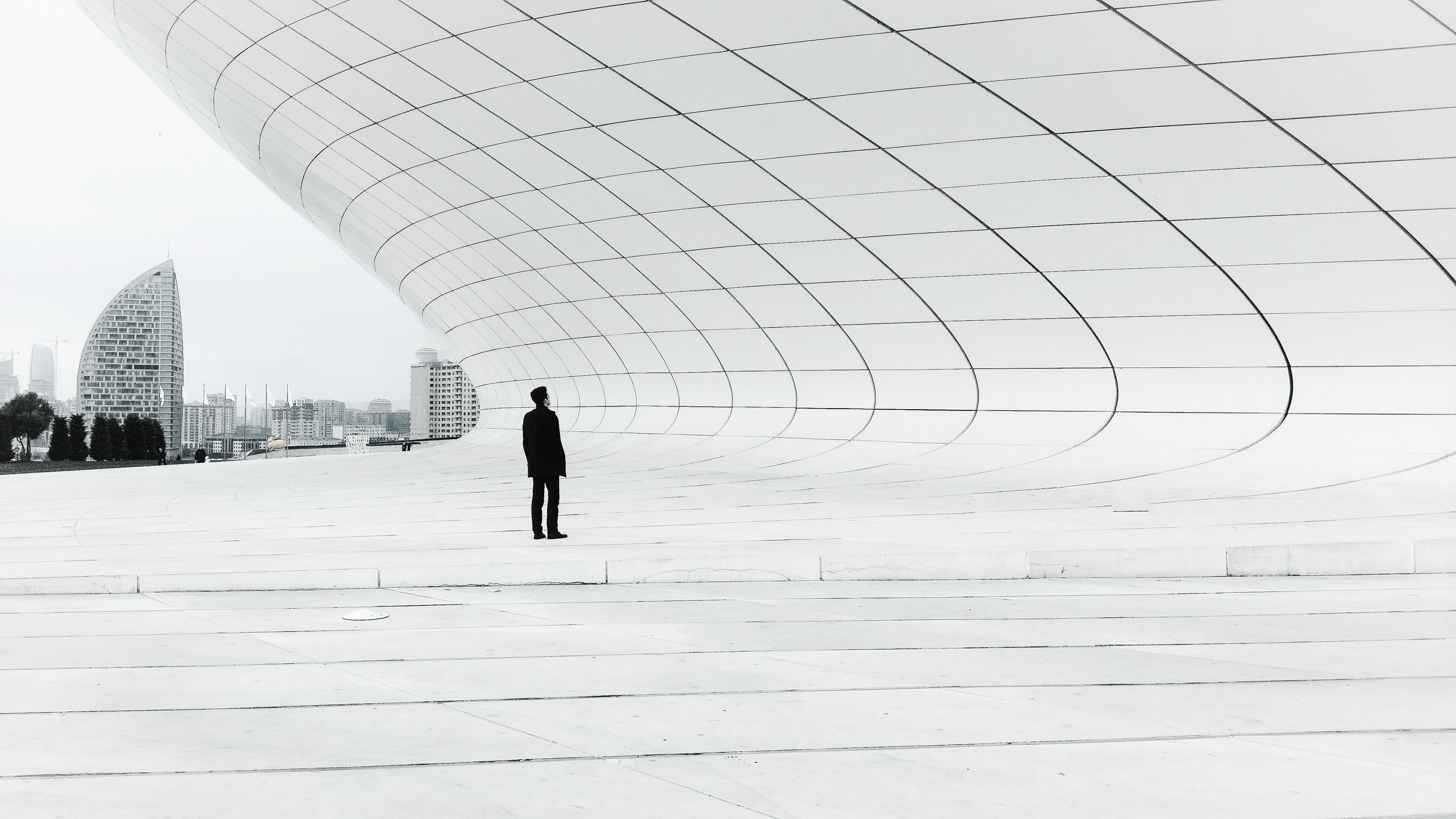 a man dressed in black standing under a wave like white concrete structure, mrblack and mrs_white 4k, HD Wallpaper