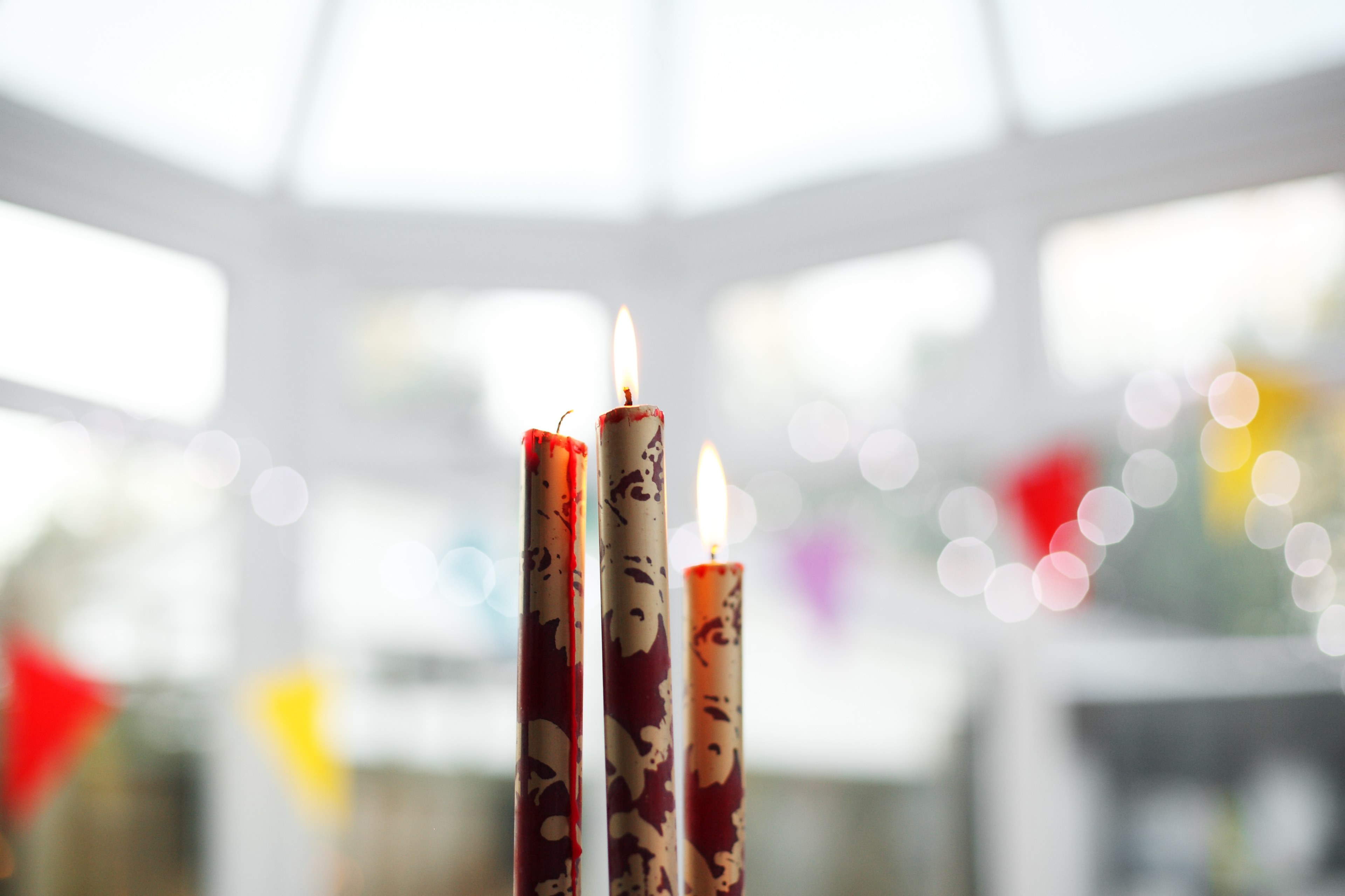 macro of three tall red lit candlesticks under a giant white windowed building adorned with string lights, red candlesticks 4k, HD Wallpaper