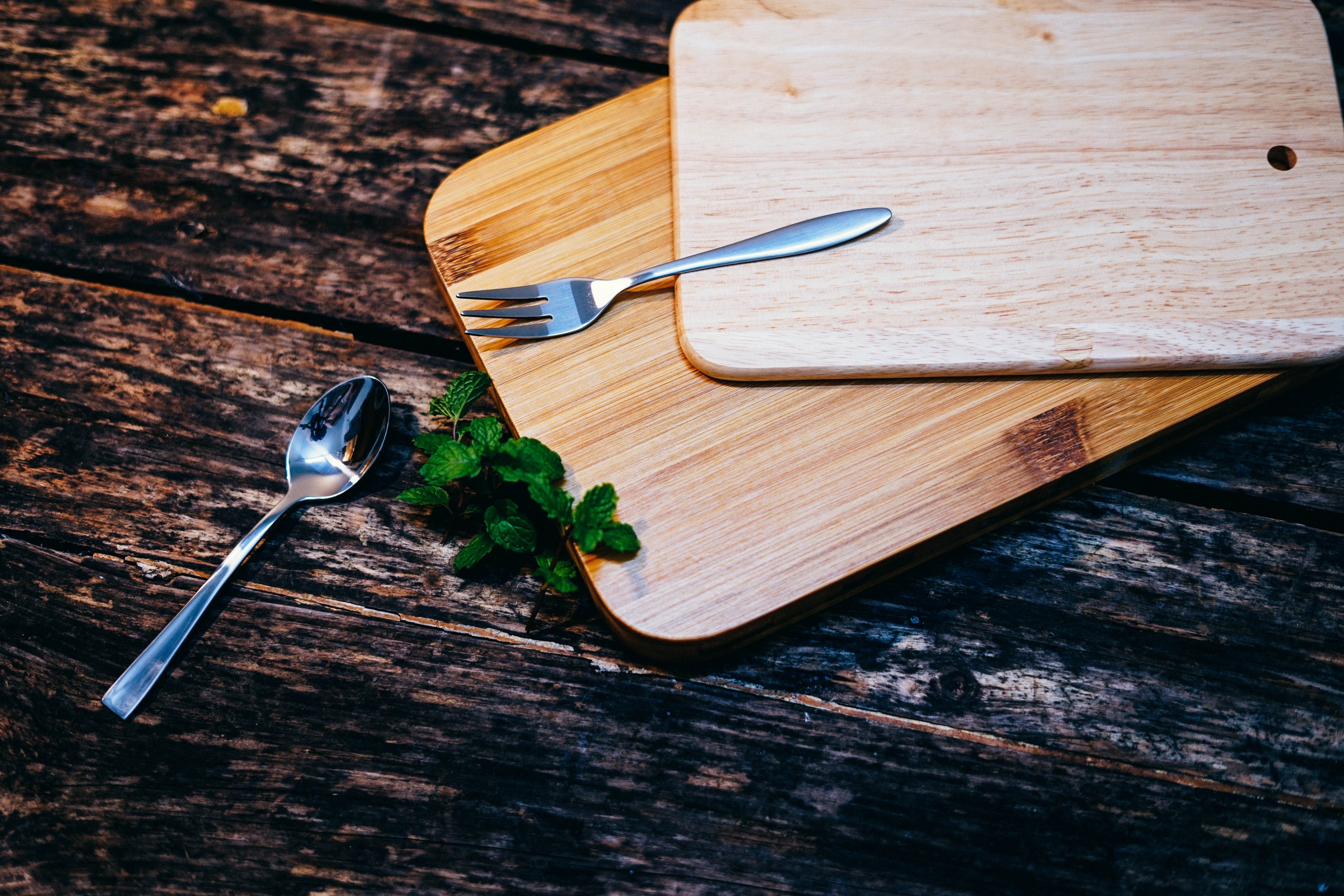 two wooden chopping boards on top of each other beside leaves of mint and a metal spoon and fork, cutting boards and cutlery 4k, HD Wallpaper
