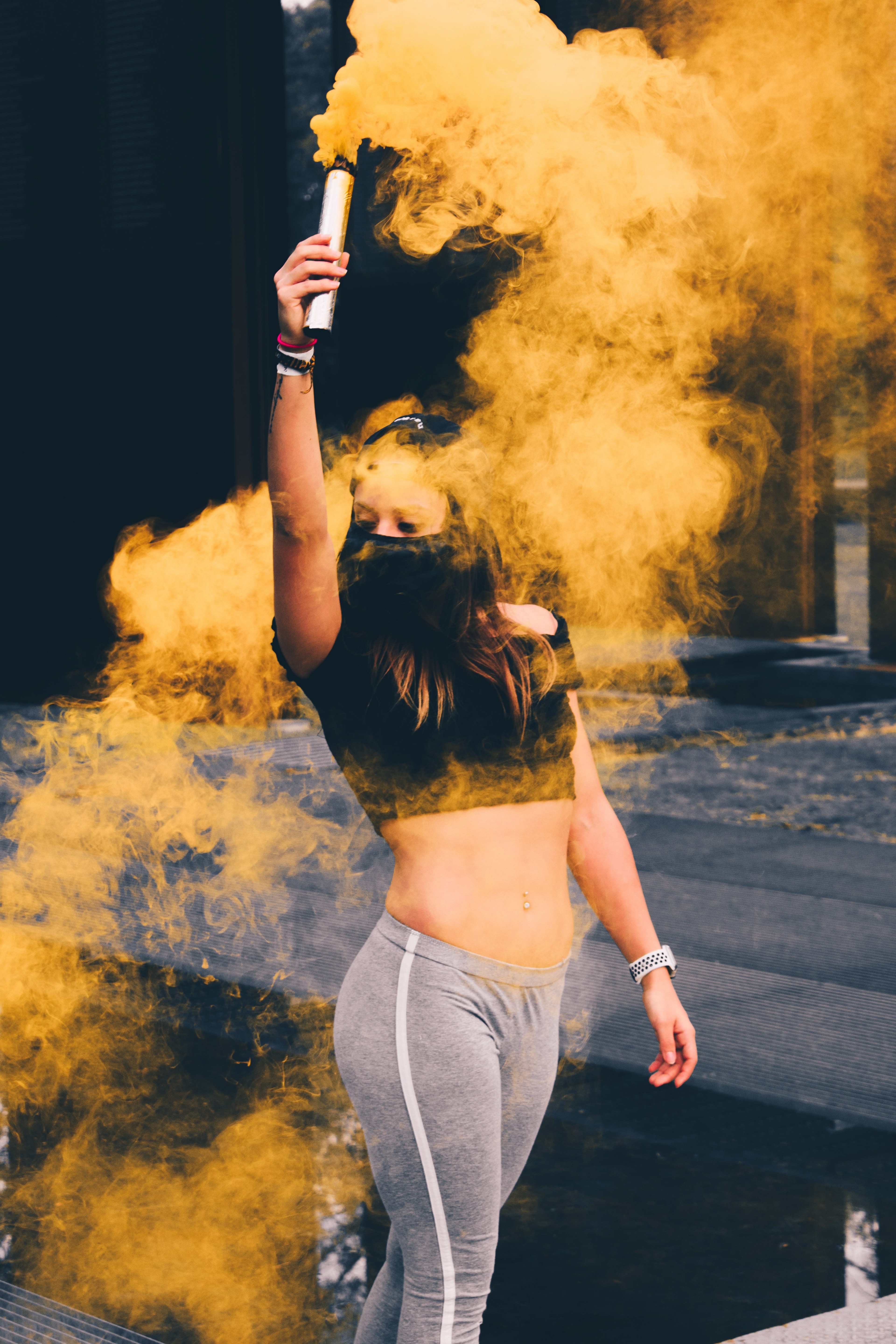 a performer in a midriff top and gray athletic pants holds up a yellow smoke grenade, urbex girl_ 4k, Phone HD Wallpaper