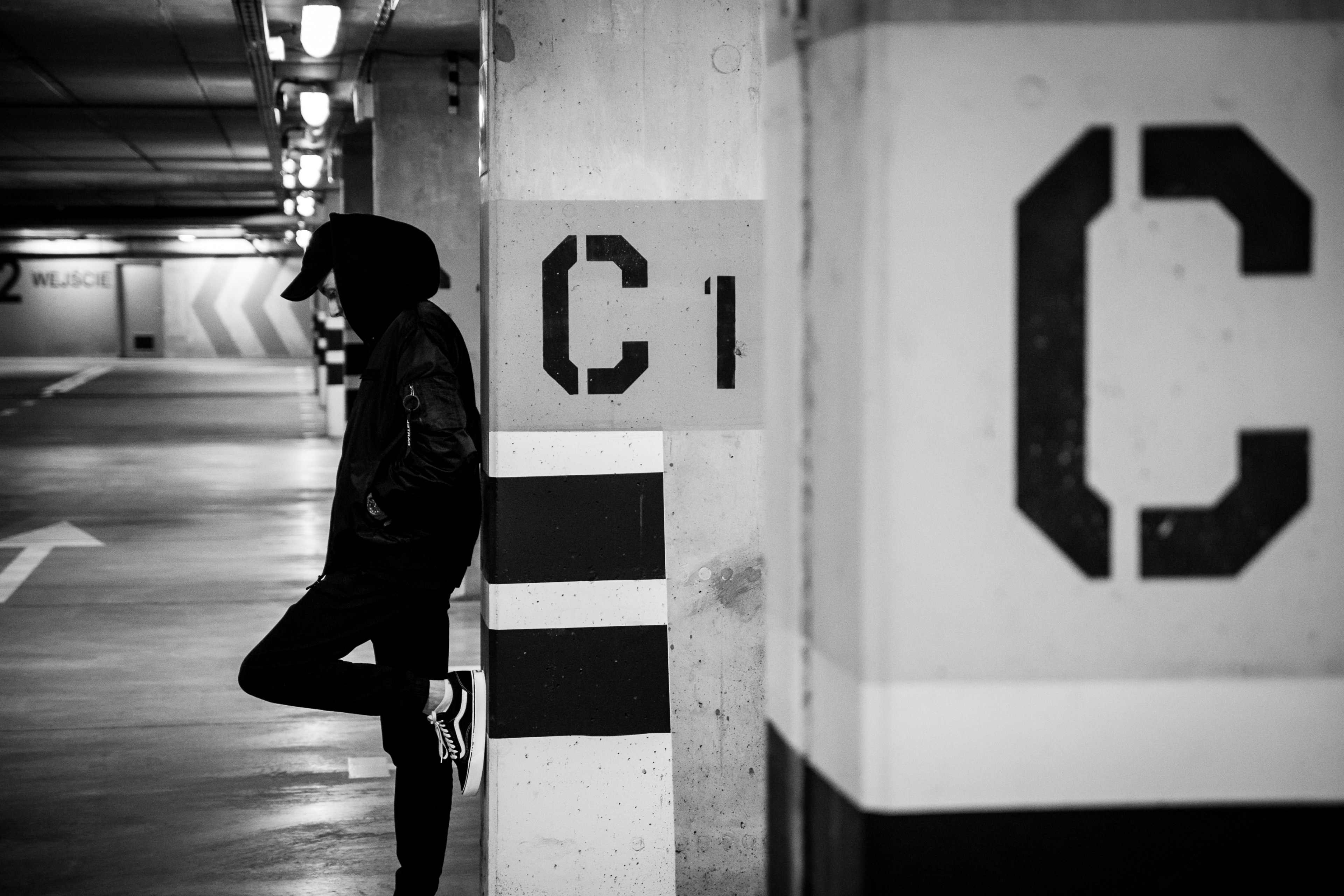 black and white shot standing and leaning against underground car park pillar with c sign, c sign and man in car park 4k, HD Wallpaper