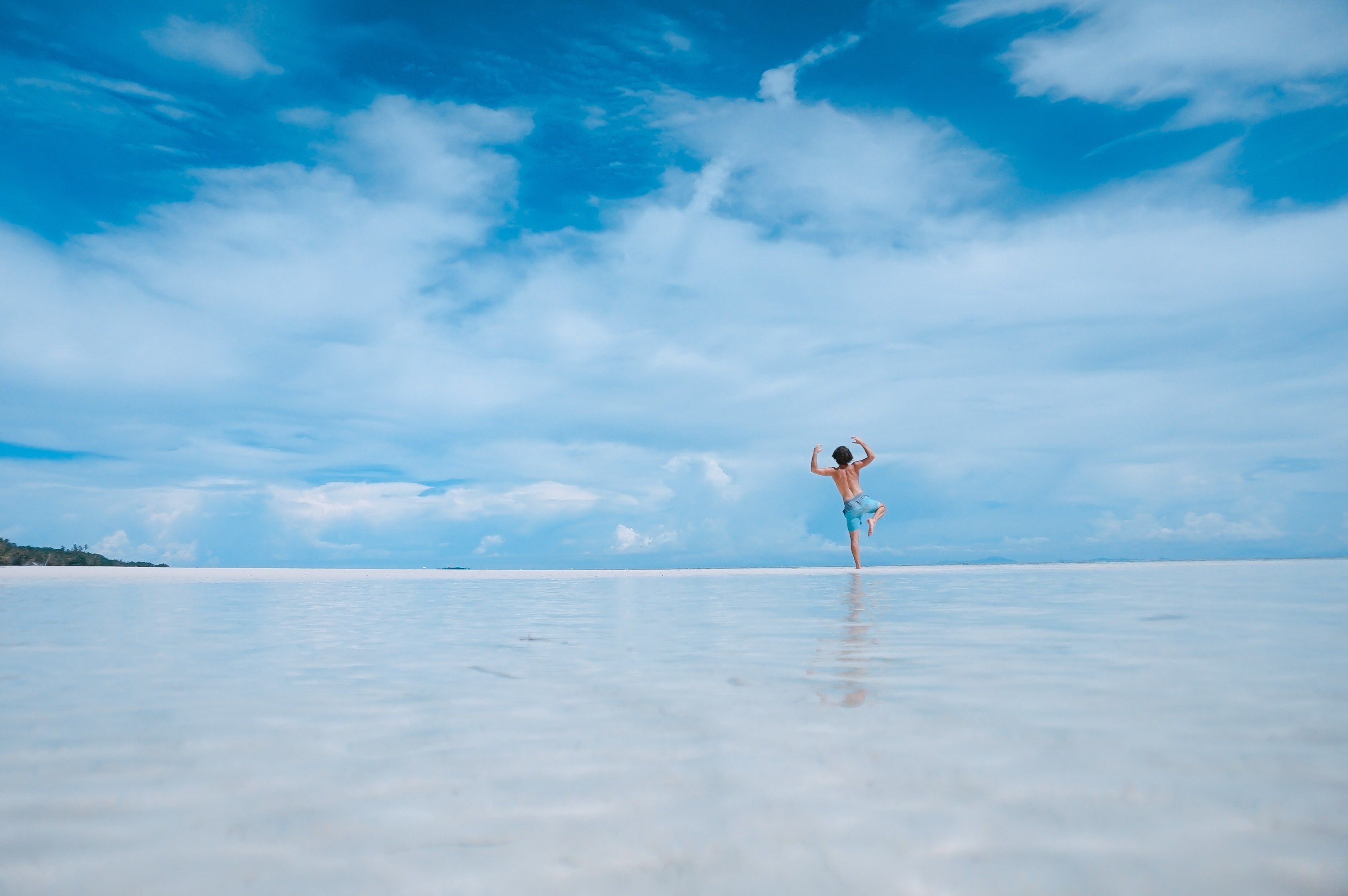 a low shot of a young man standing on one leg and raising his hands on the edge of a beach, balancing in the sea water 4k, HD Wallpaper