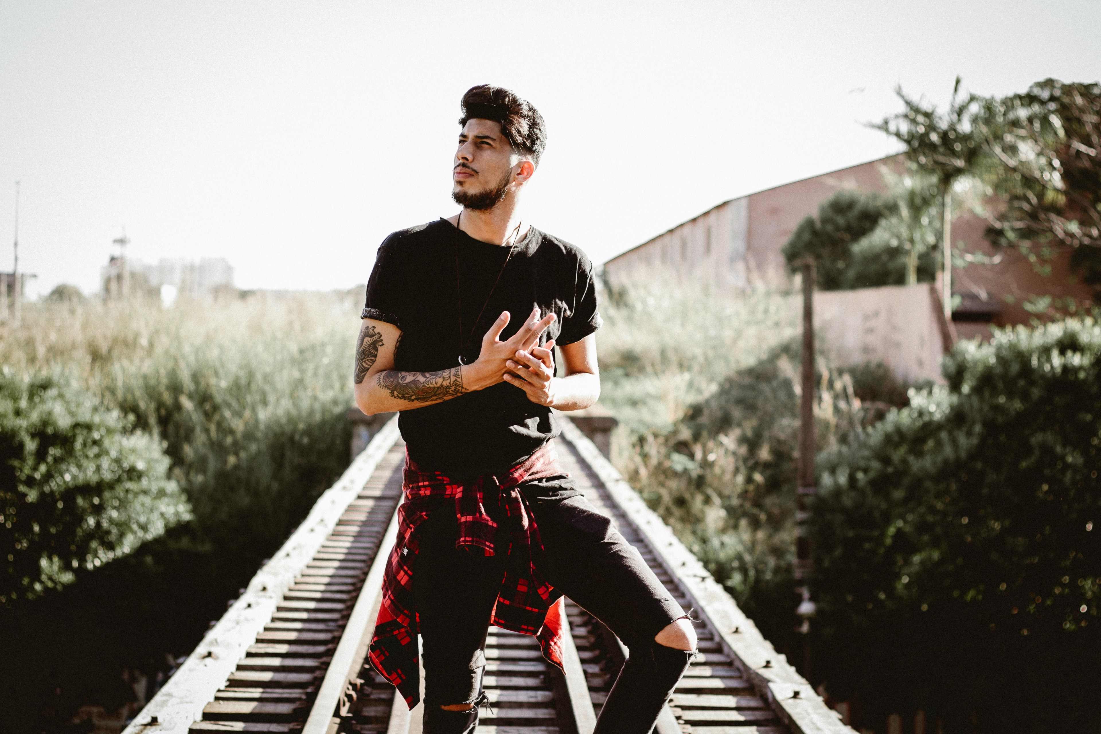 man with arm tattoos wearing a black shirt standing on a train track during the day, man standing on railroad track 4k, HD Wallpaper