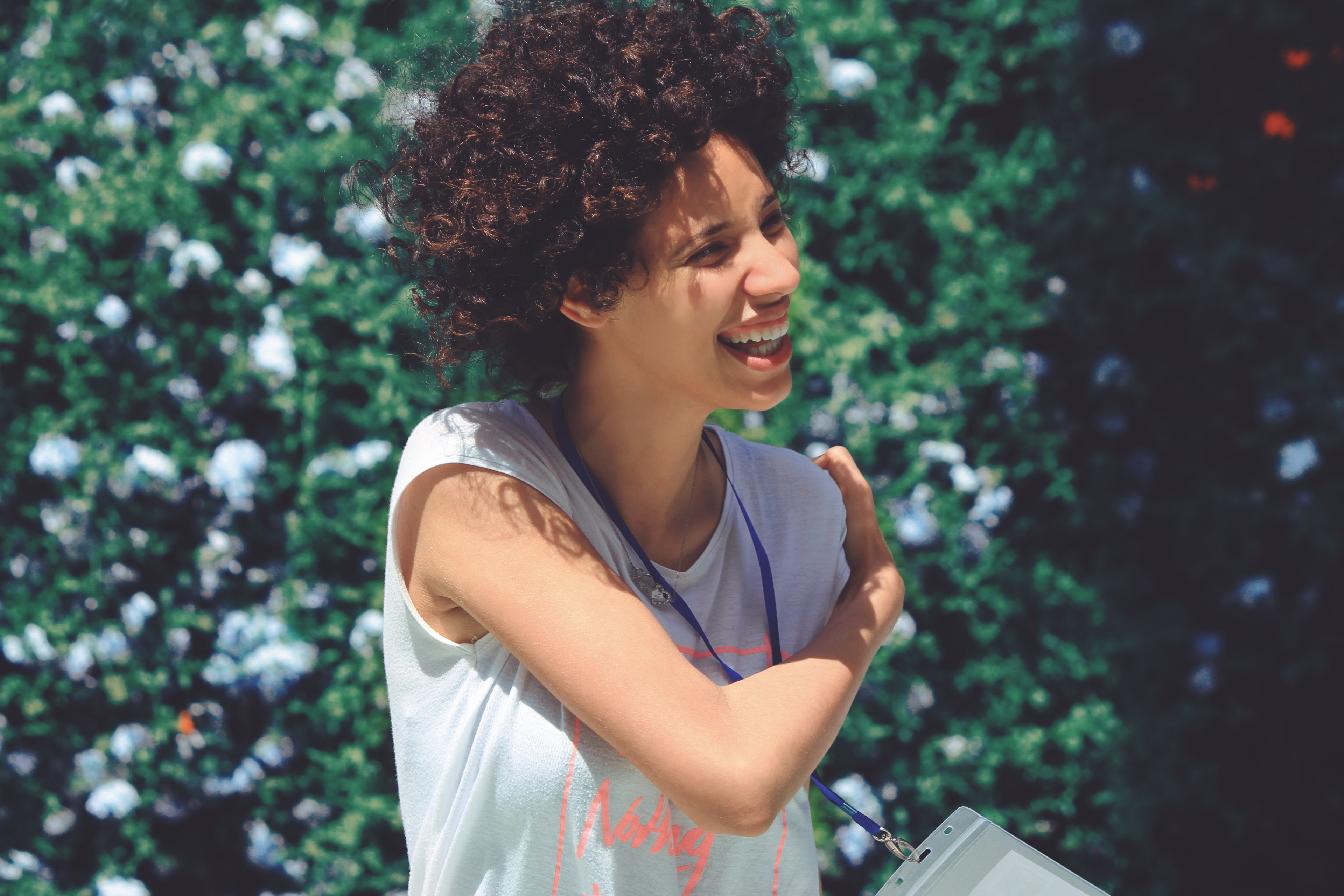 woman with curly hair laughs while wrapping her arm around to her shoulder in front of greenery, happy 4k, HD Wallpaper