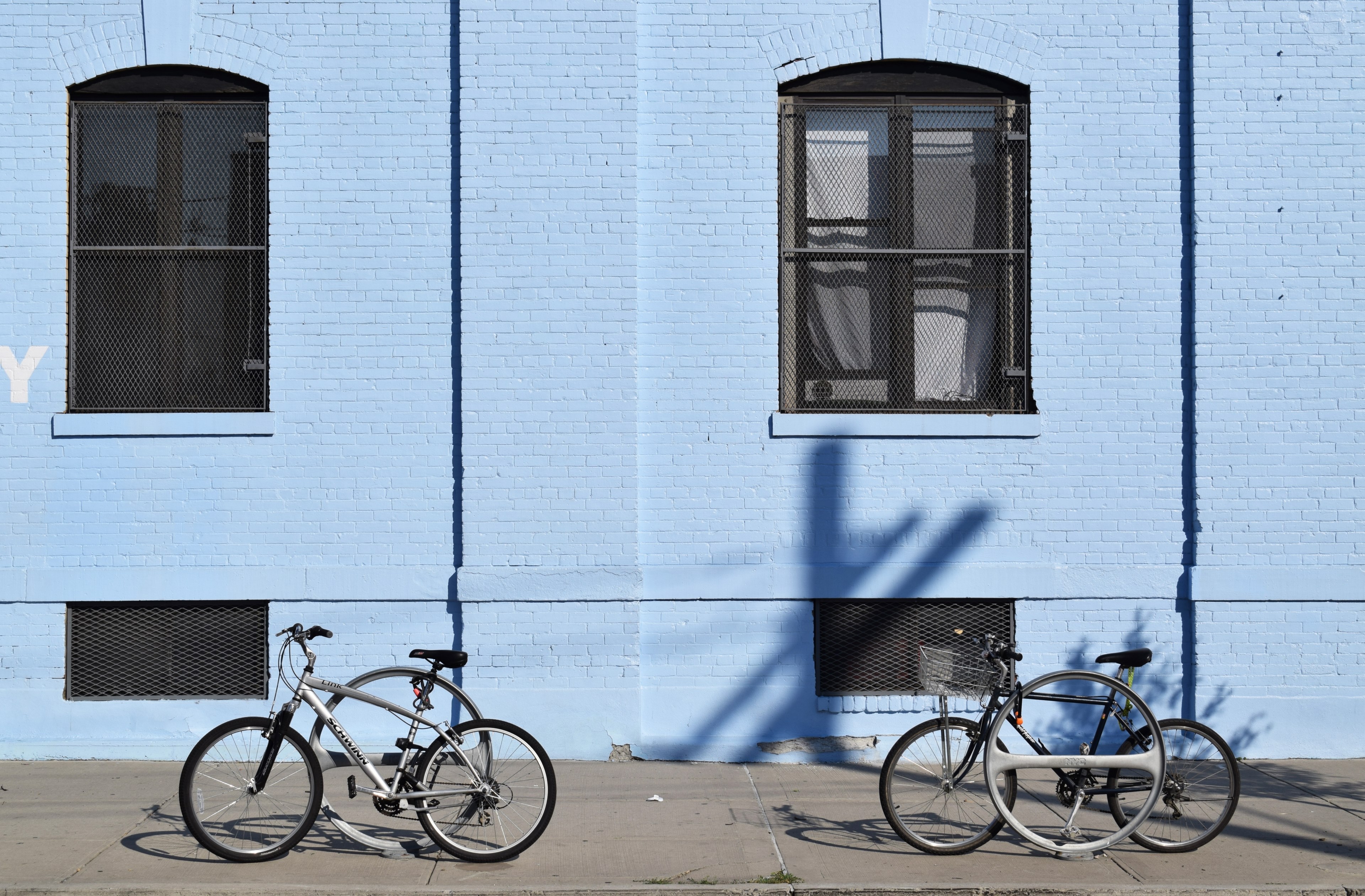 two bikes are attached to bike racks in front of light blue building with dark windows, bikes with blue building 4k, HD Wallpaper