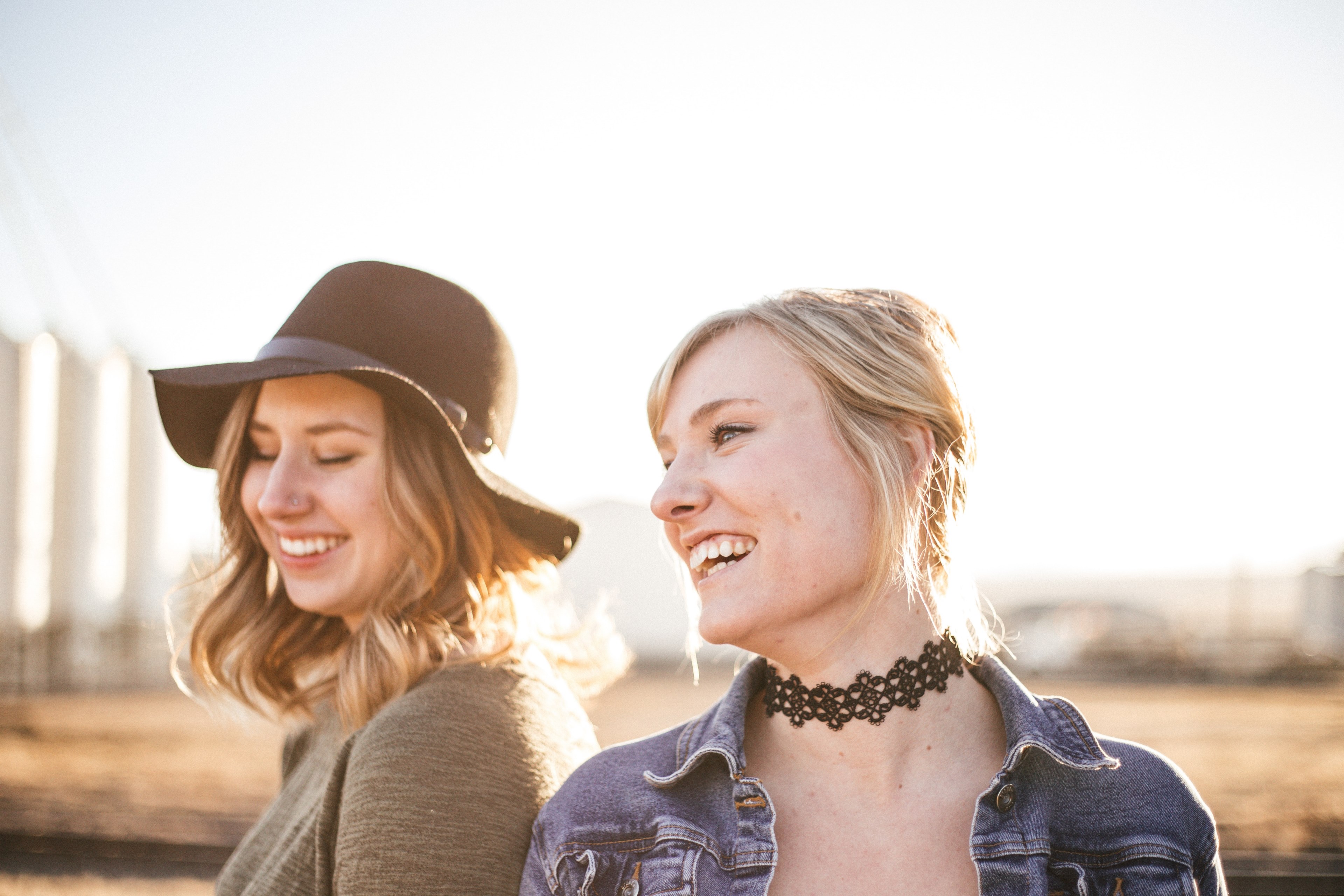 two women in a hat and choker stand closely laughing against a blurry outdoor background, women with hat and choker 4k, HD Wallpaper