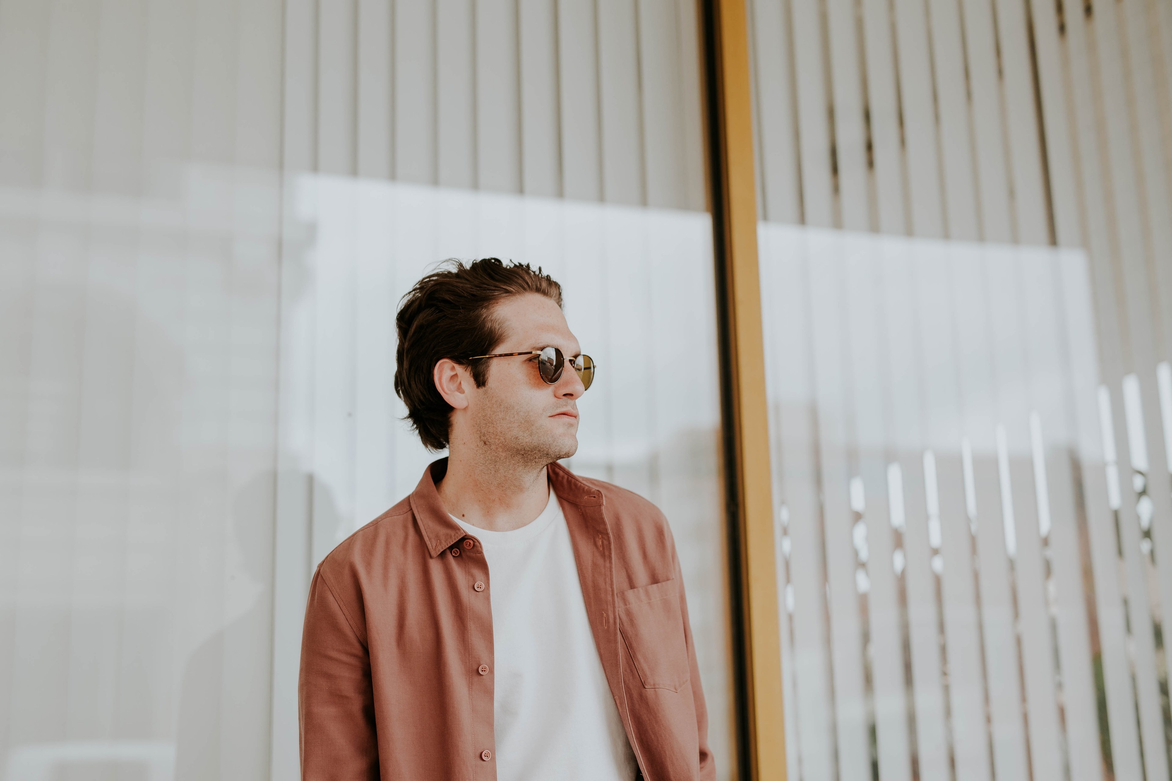 a happy looking man with an orange coat and sunglasses staring at the scenery near a building with large windows, _man orange coat 4k, HD Wallpaper