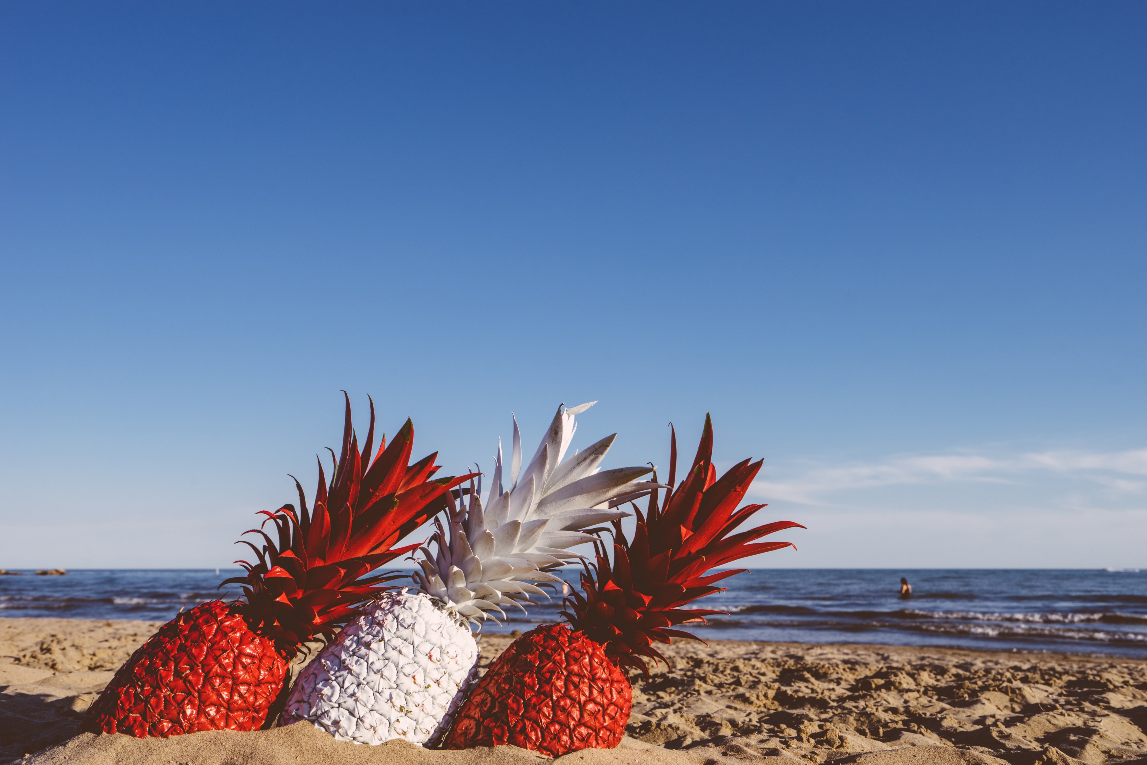 a close up of three pineapples painted red and white sticking out of the beach sand, red and white pineapples 4k, HD Wallpaper