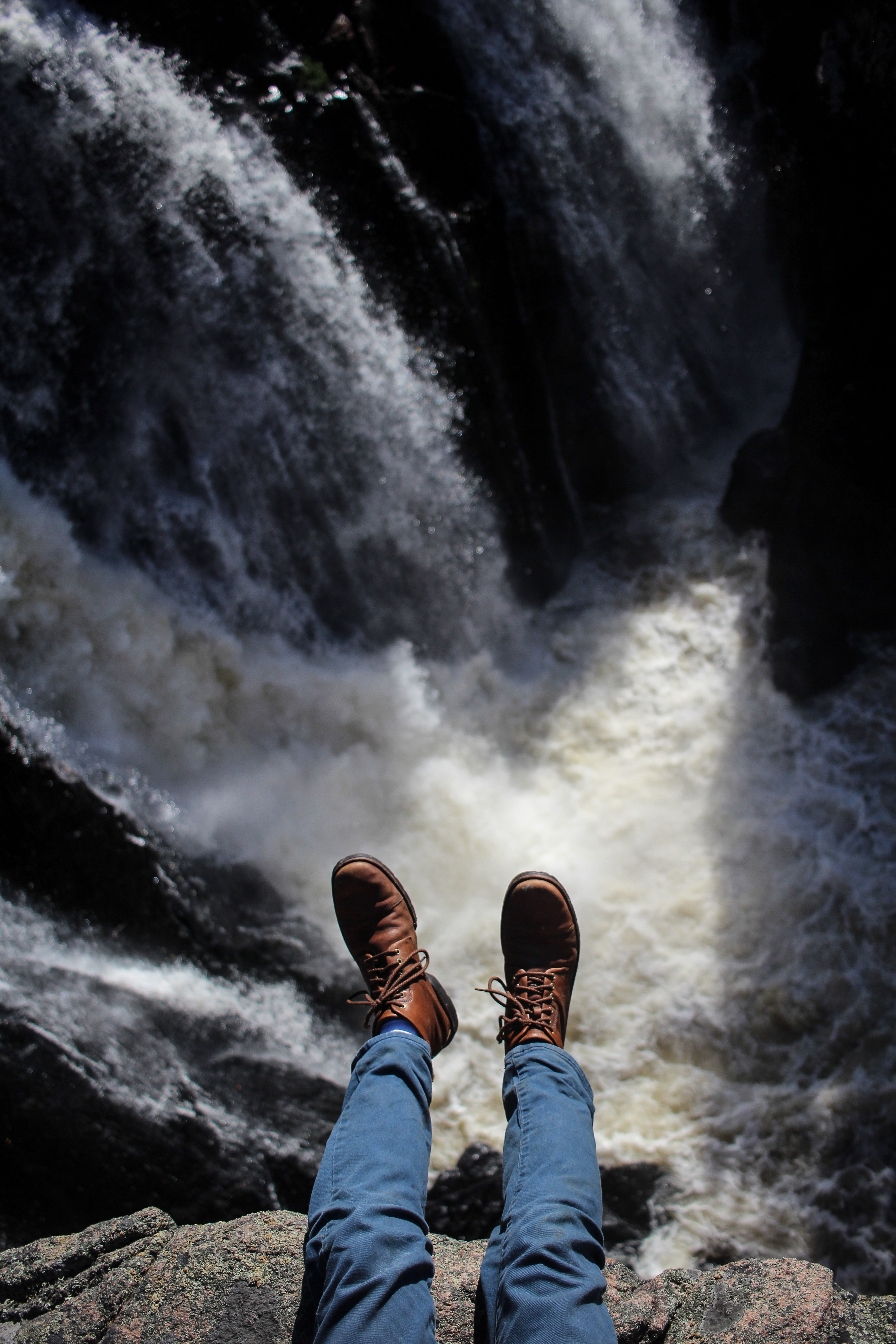 a males legs in blue pants and boots hanging over the side of a waterfall, shoes and waterfall 4k, Phone HD Wallpaper