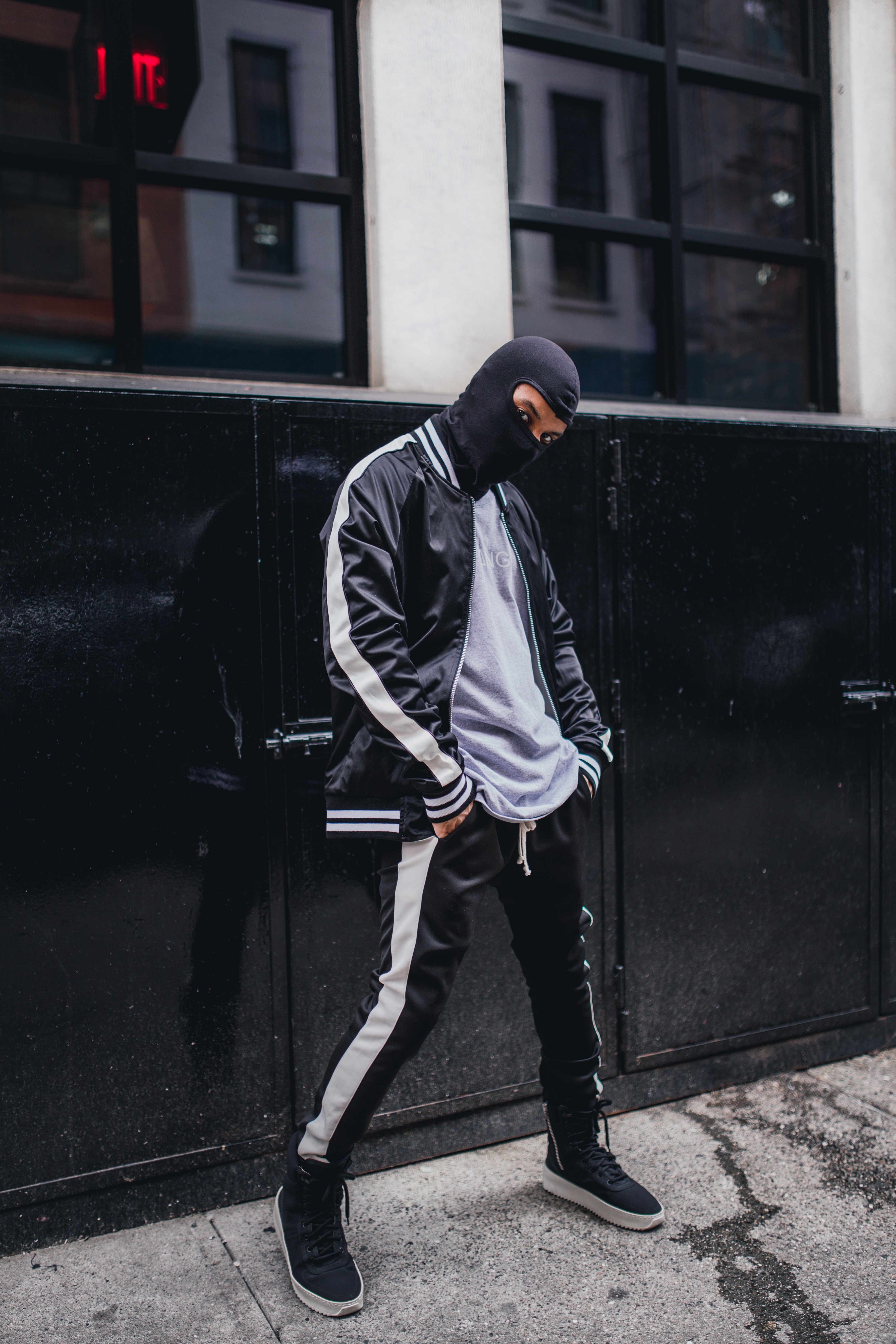 a man wearing a mask in a black tracksuit poses in front of a black and white building, man in a black mask 4k, Phone HD Wallpaper