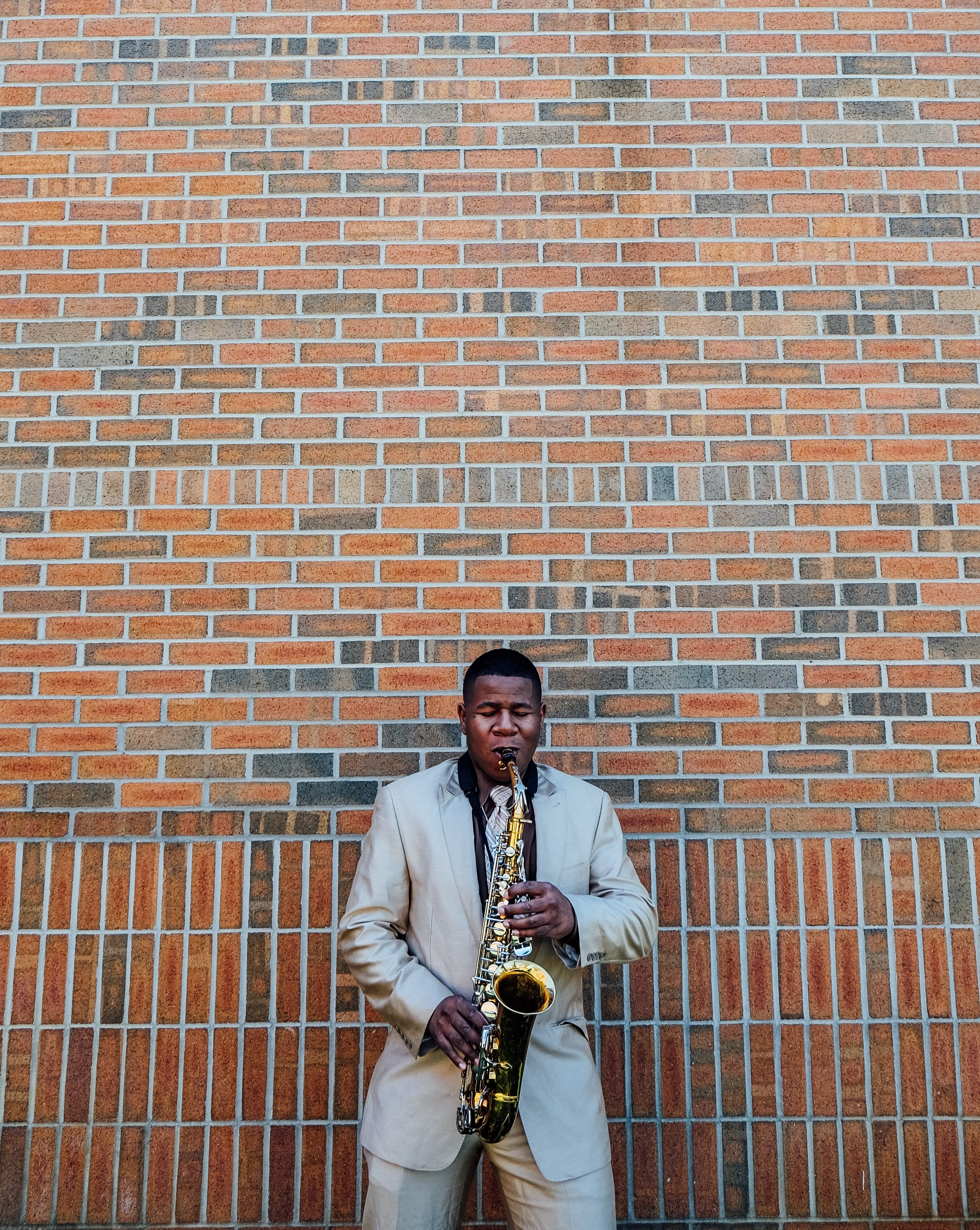 a man in a glossy silver suit playing the saxophone against a brick wall, elegant saxophone player 4k, Phone HD Wallpaper