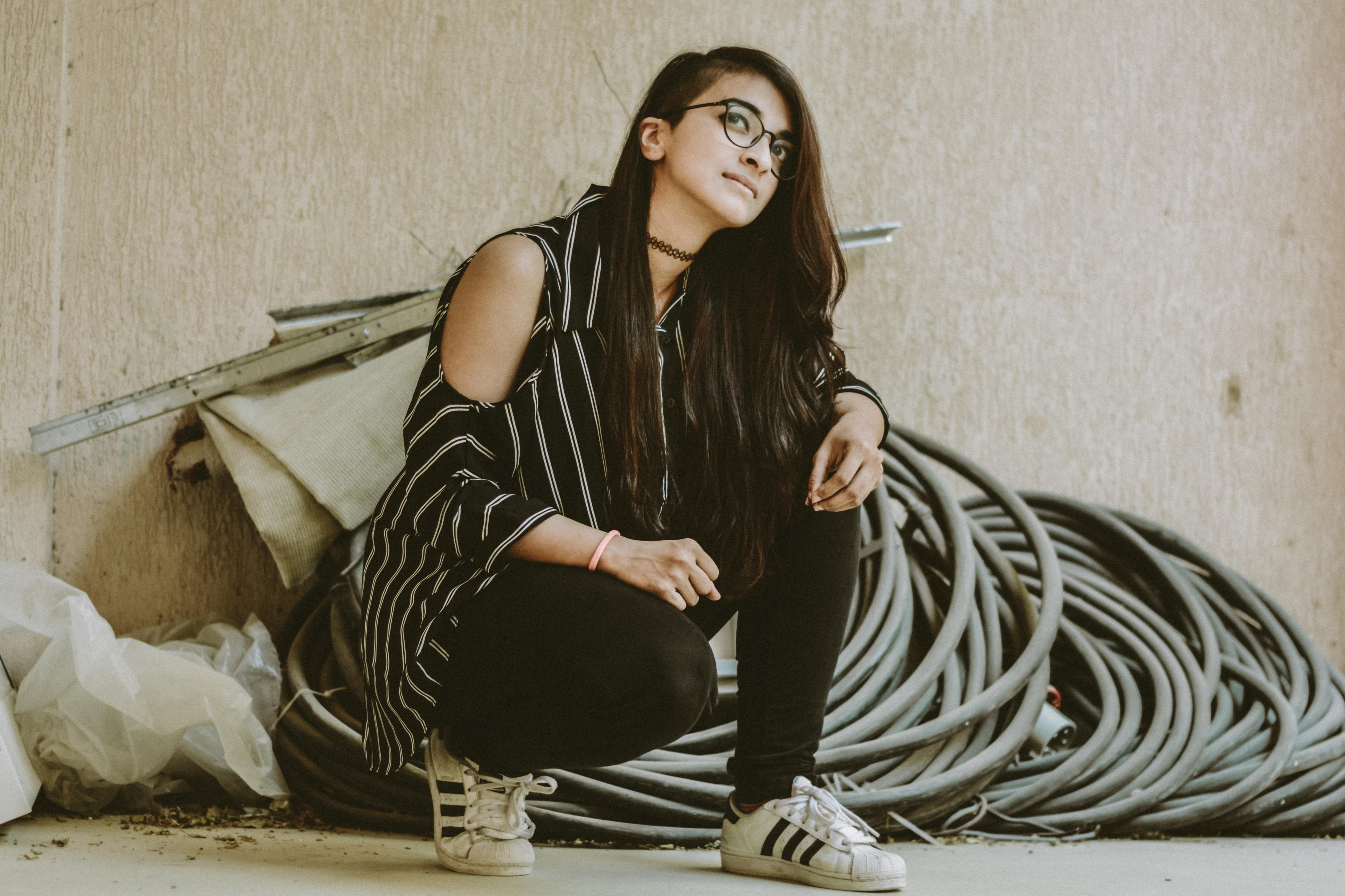 a woman with glasses in adidas kneels looking upward by piping and building materials, woman with piping 4k, HD Wallpaper