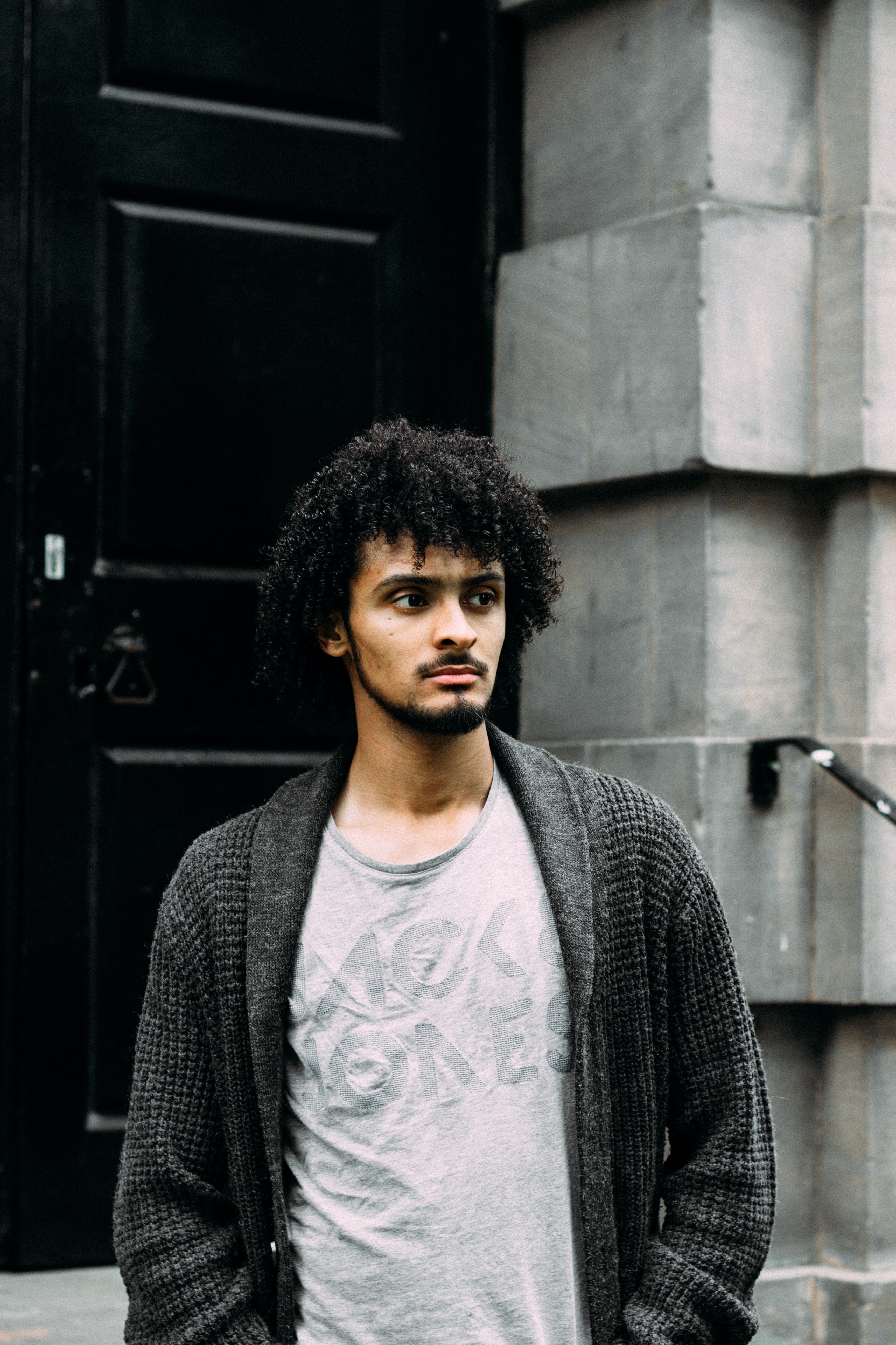 man with curly hair standing alone outside a building doorway, gray scale 4k, Phone HD Wallpaper