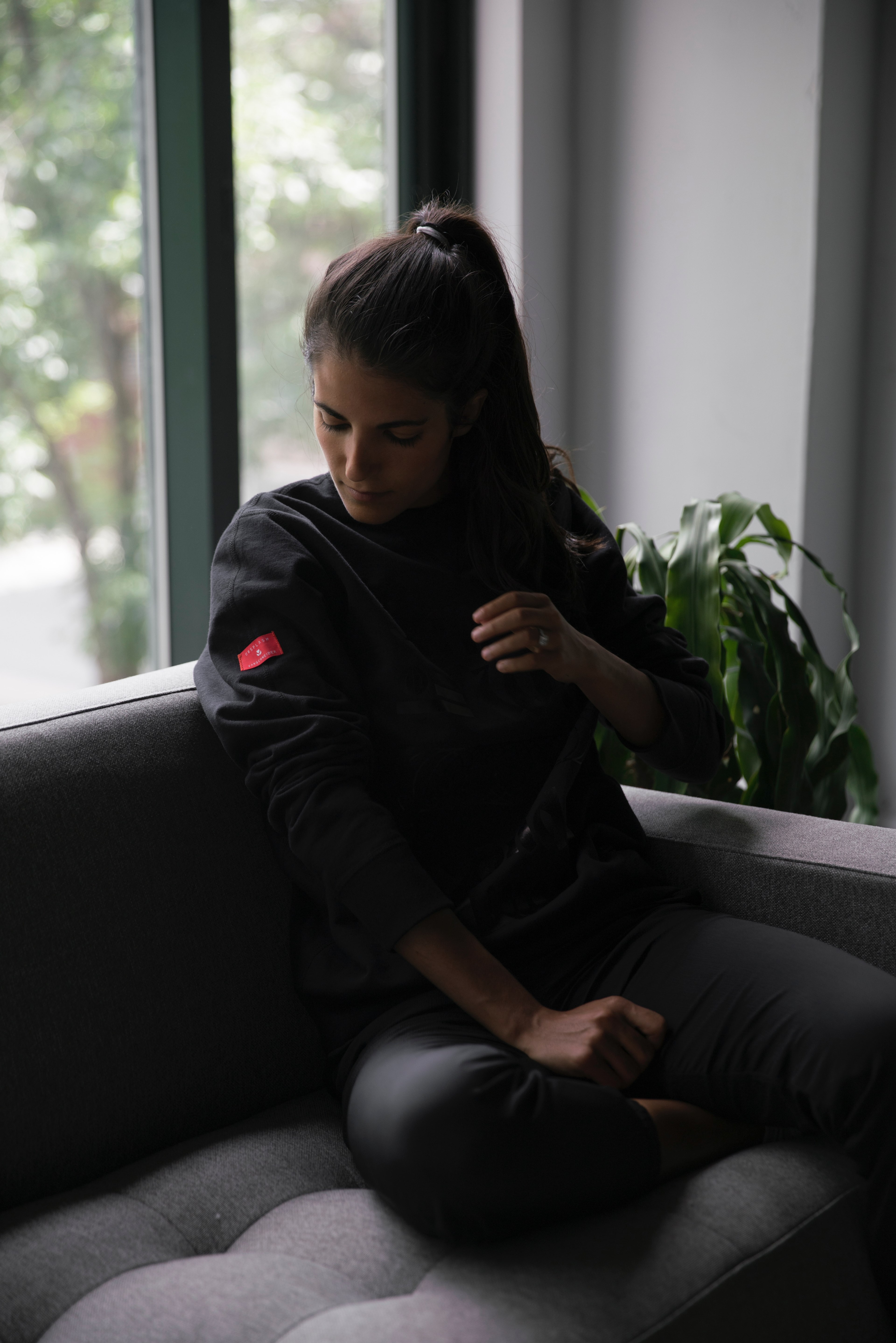woman on the couch looking at the logo on her sweater sleeve, the urban explorer sweatshirt 4k, Phone HD Wallpaper