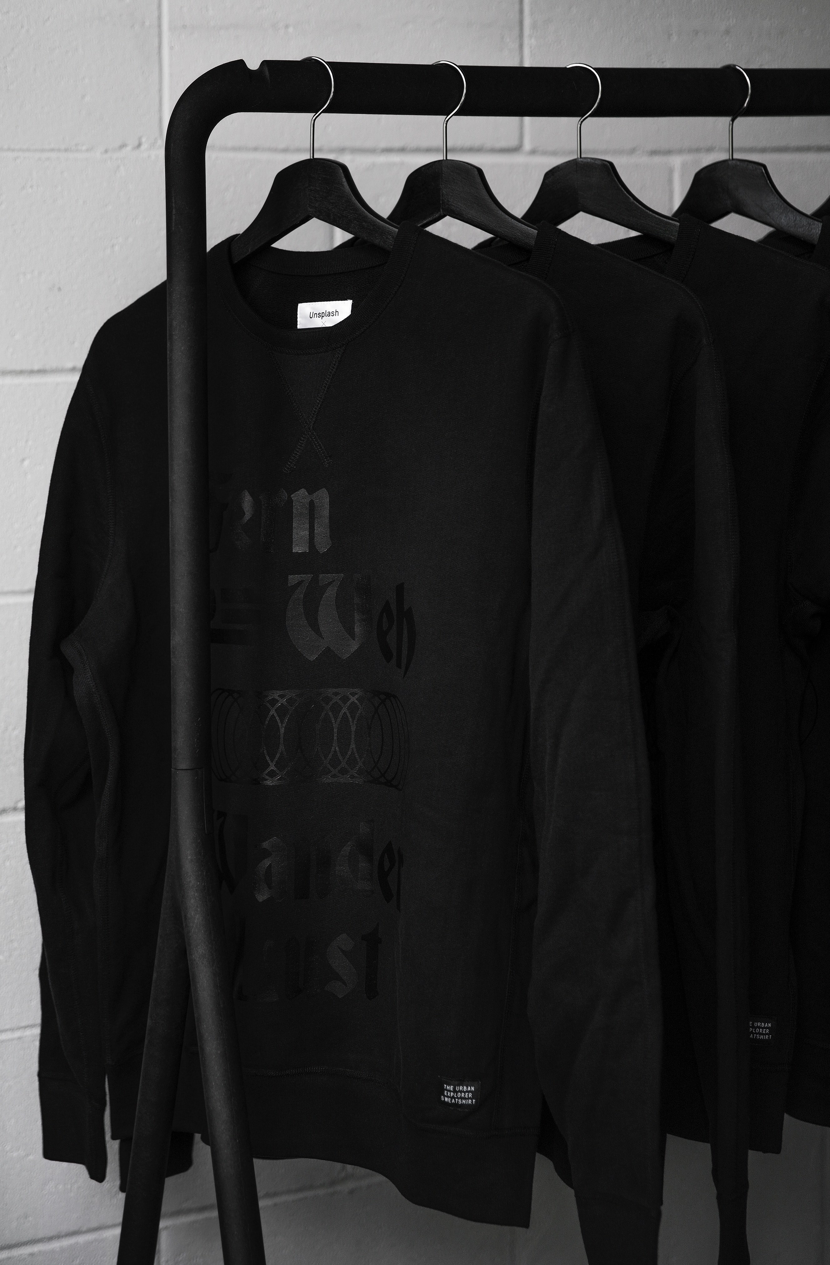 black sweatshirts hang from black hangs on a rack against a white brick wall, the urban explorer sweatshirt 4k, Phone HD Wallpaper