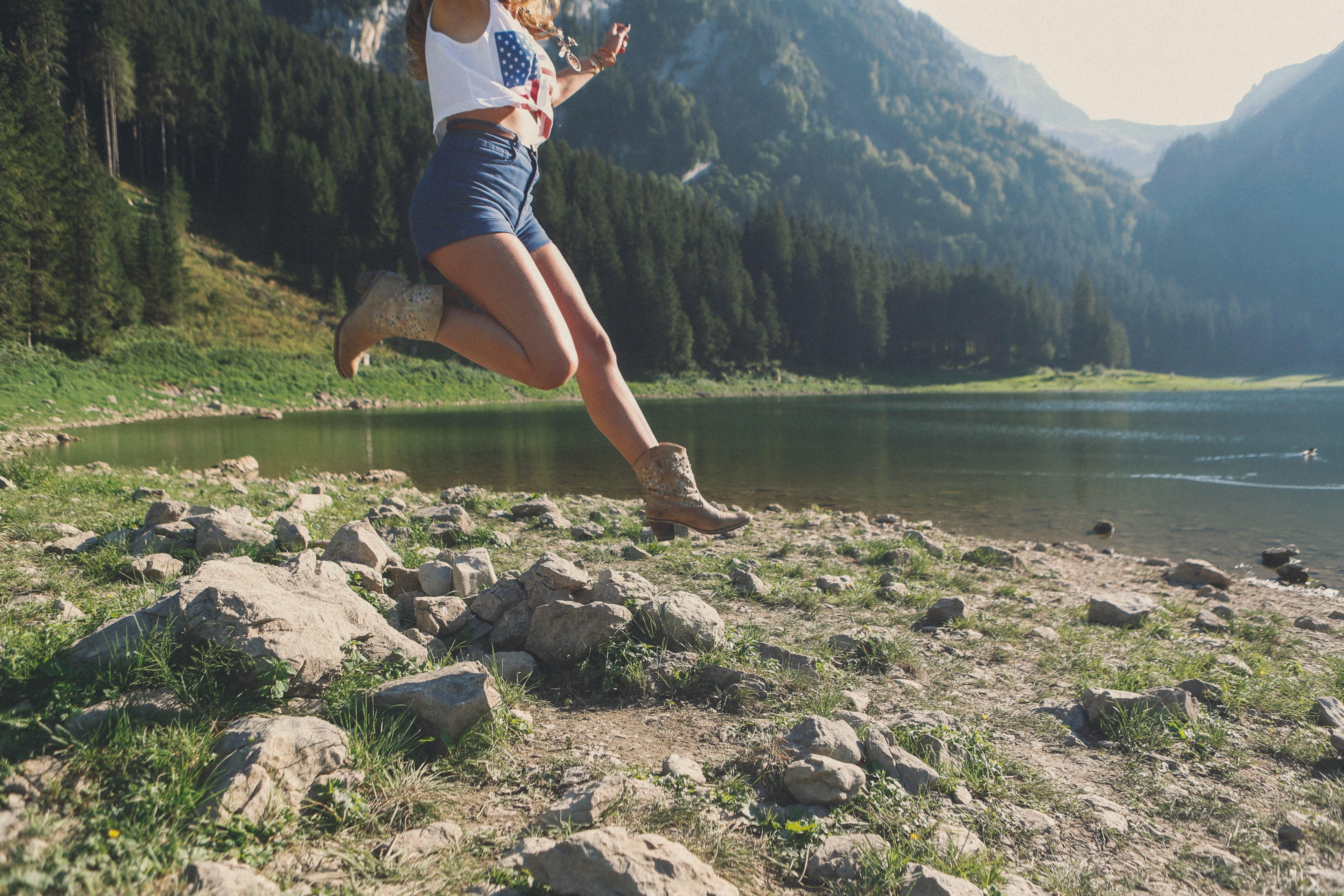 a woman in cowboy boots jumping over rocks on a shore of a mountain lake, leaping woman by a lake 4k, HD Wallpaper