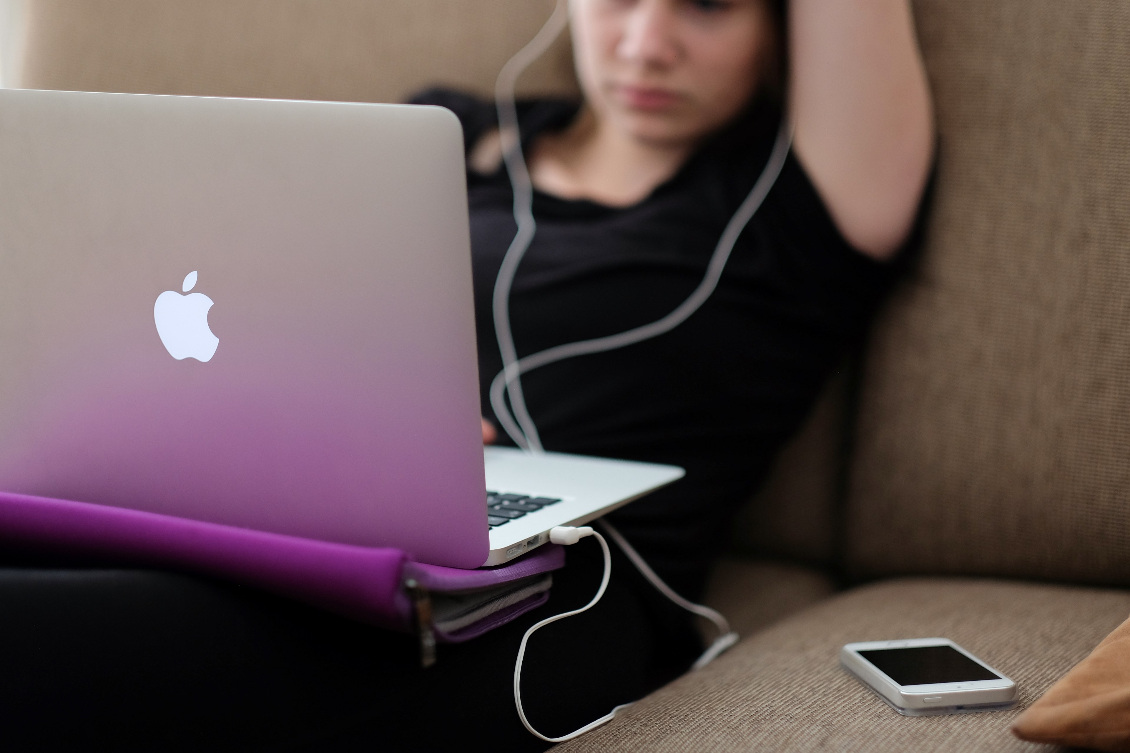 a woman using a macbook on a sofa with a white iphone nearby, woman with a macbook on a sofa 4k, HD Wallpaper