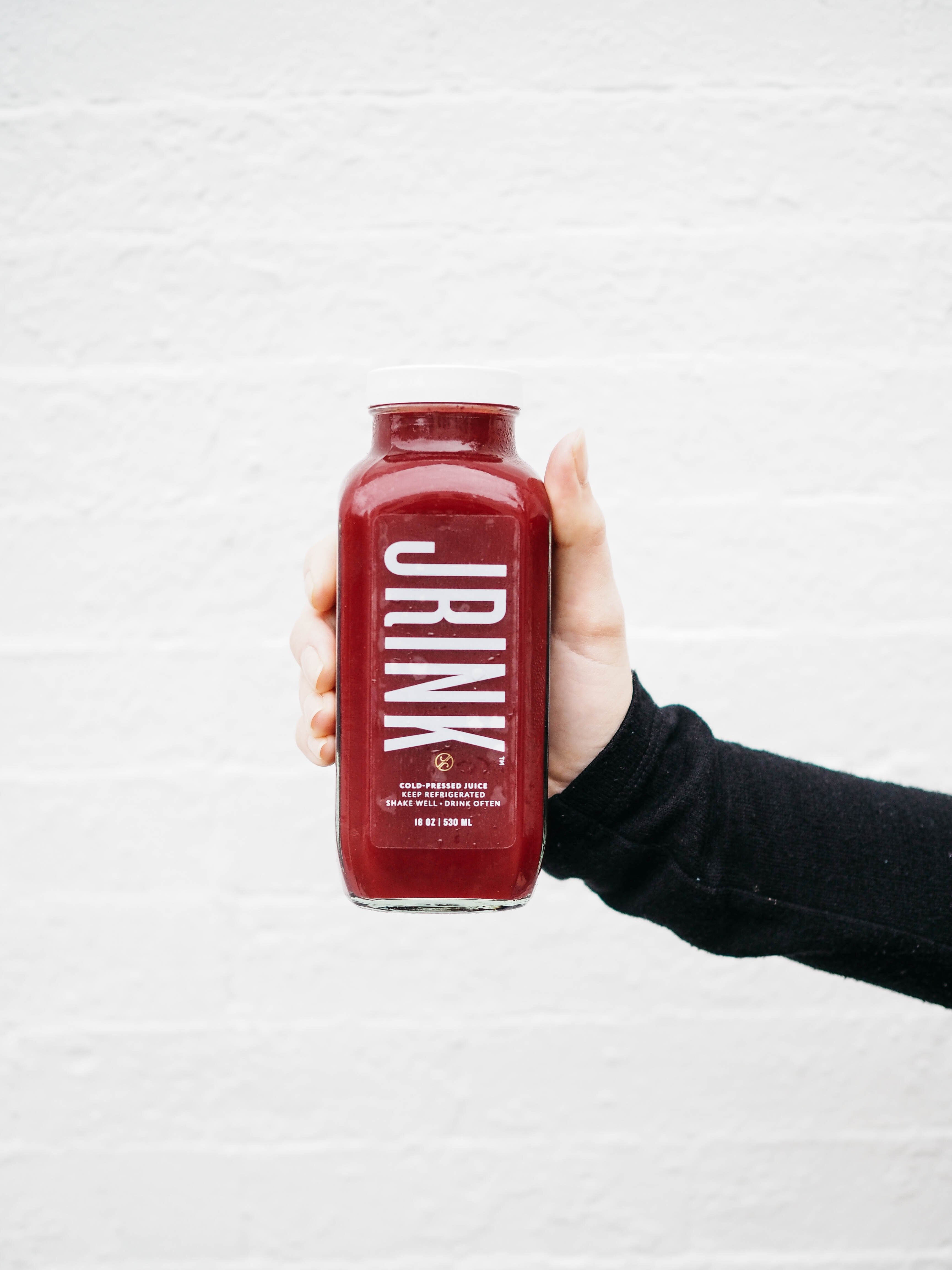 outstretched hand holds a bottle of red juice by a white brick wall, cold pressed health drink 4k, Phone HD Wallpaper