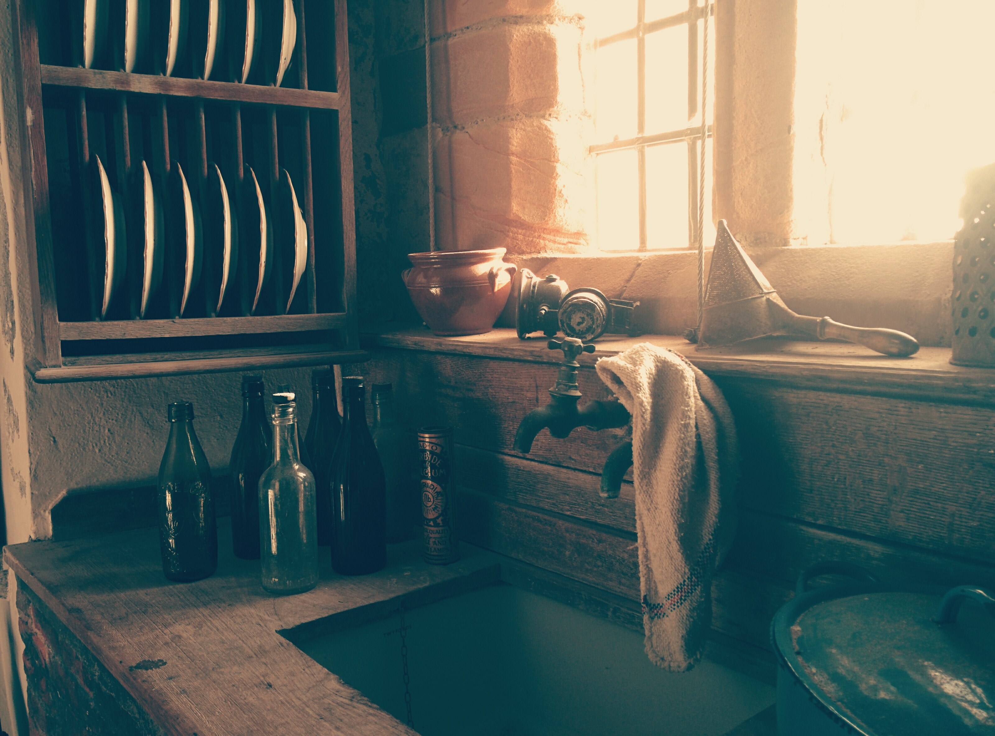 a rustic sink with bottles next to it plates on a shelf and a rag on the faucet, sink supplies 4k, HD Wallpaper