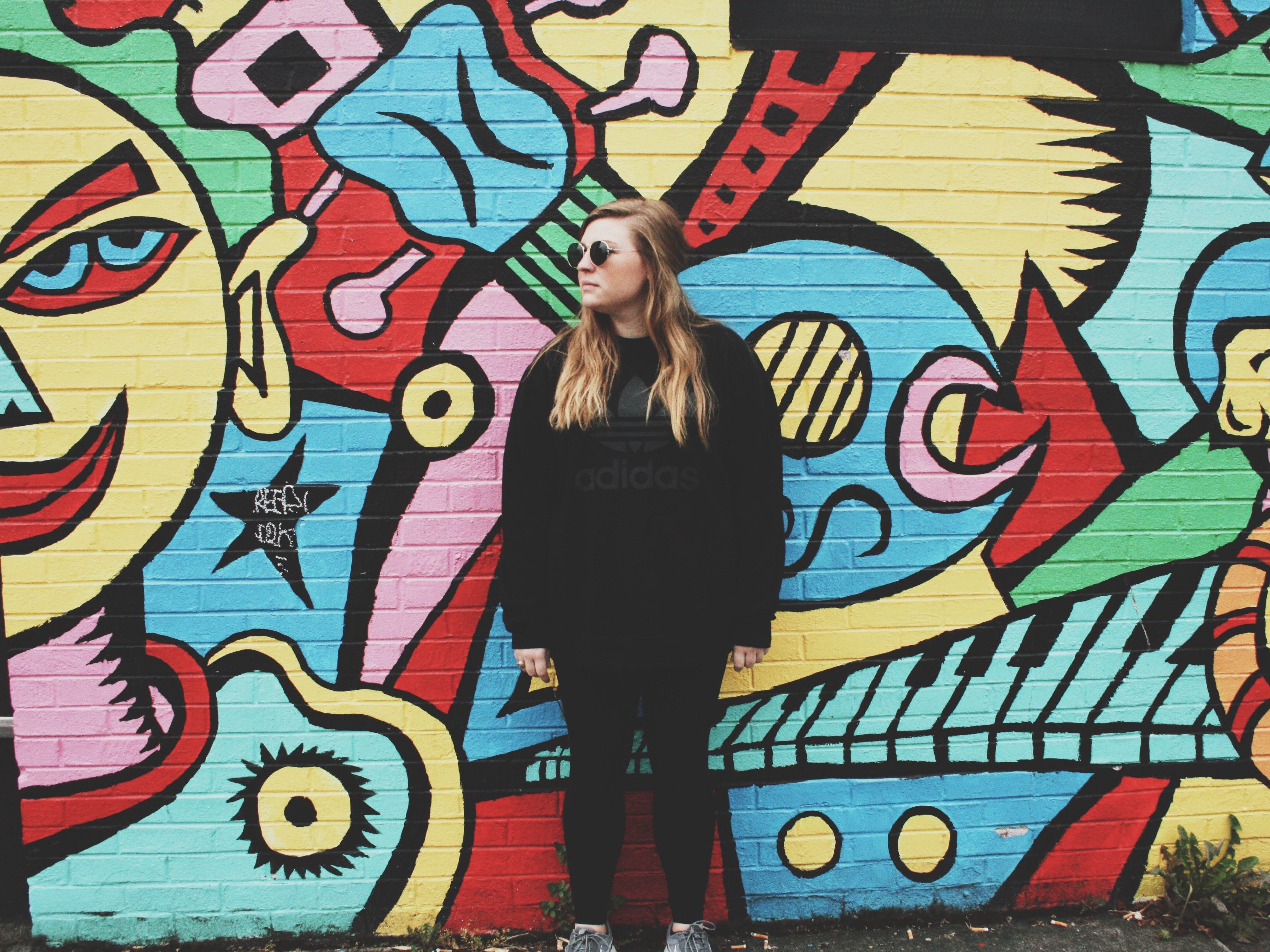 portland woman wearing all black and sunglasses stands in front of colorful graffiti mural on brick wall, woman stands in front of bright graffiti 4k, HD Wallpaper