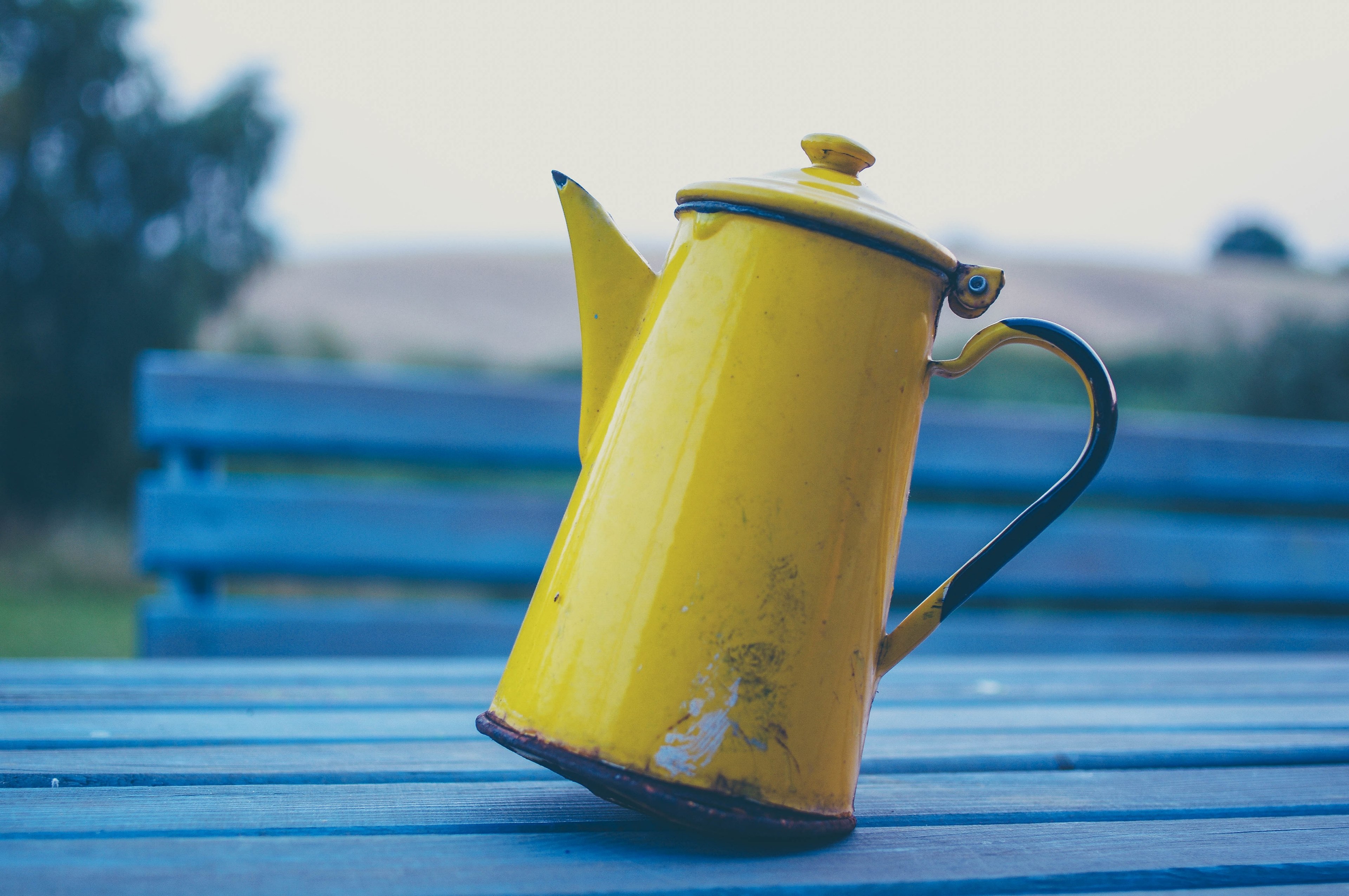 yellow teapot tipping on its handle side balancing on a blue outdoor table, yellow coffee pot 4k, HD Wallpaper