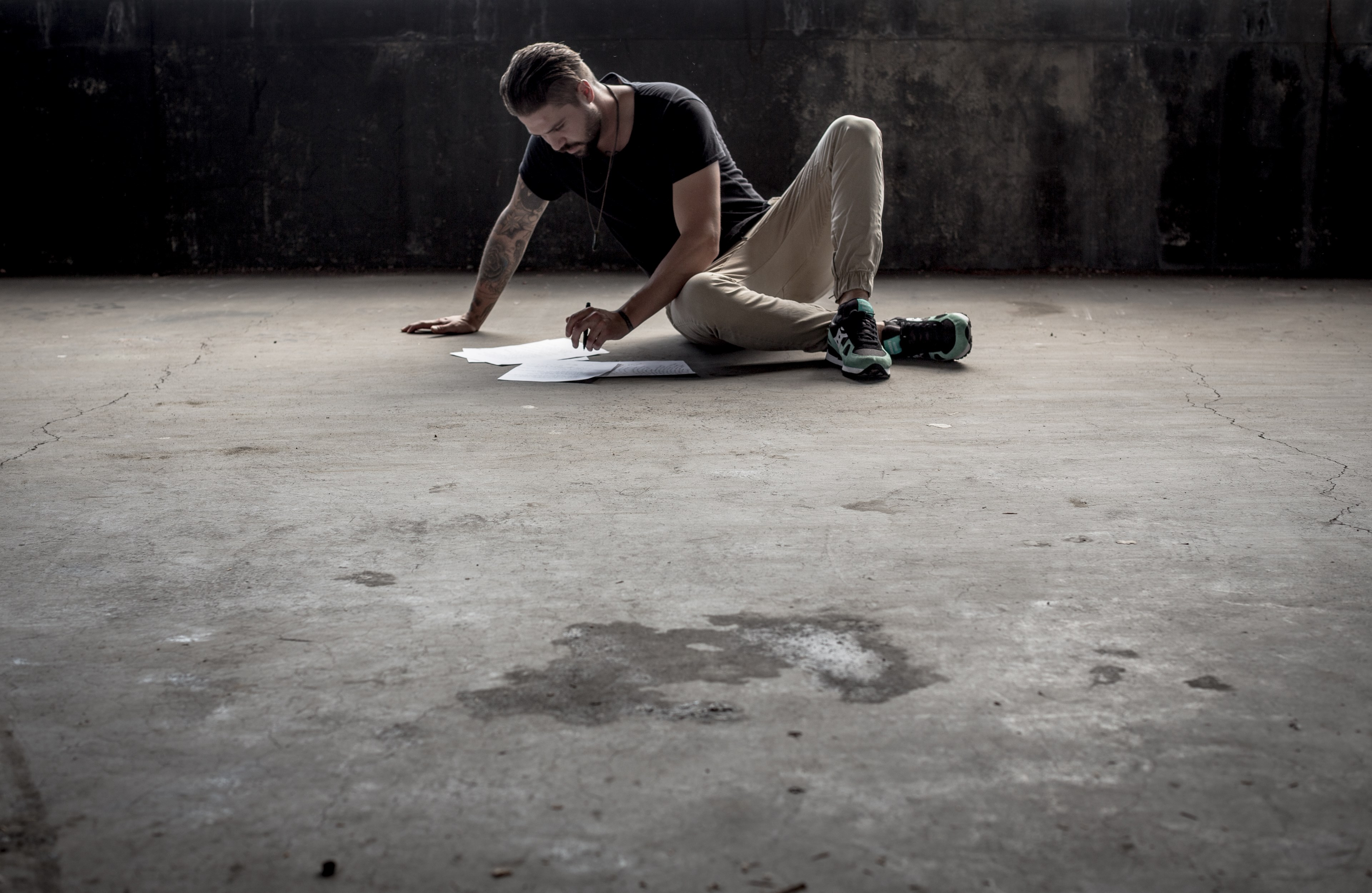 a man with a pen looking at sheets of paper while seated on a concrete industrial floor, man writing on concrete floor 4k, HD Wallpaper