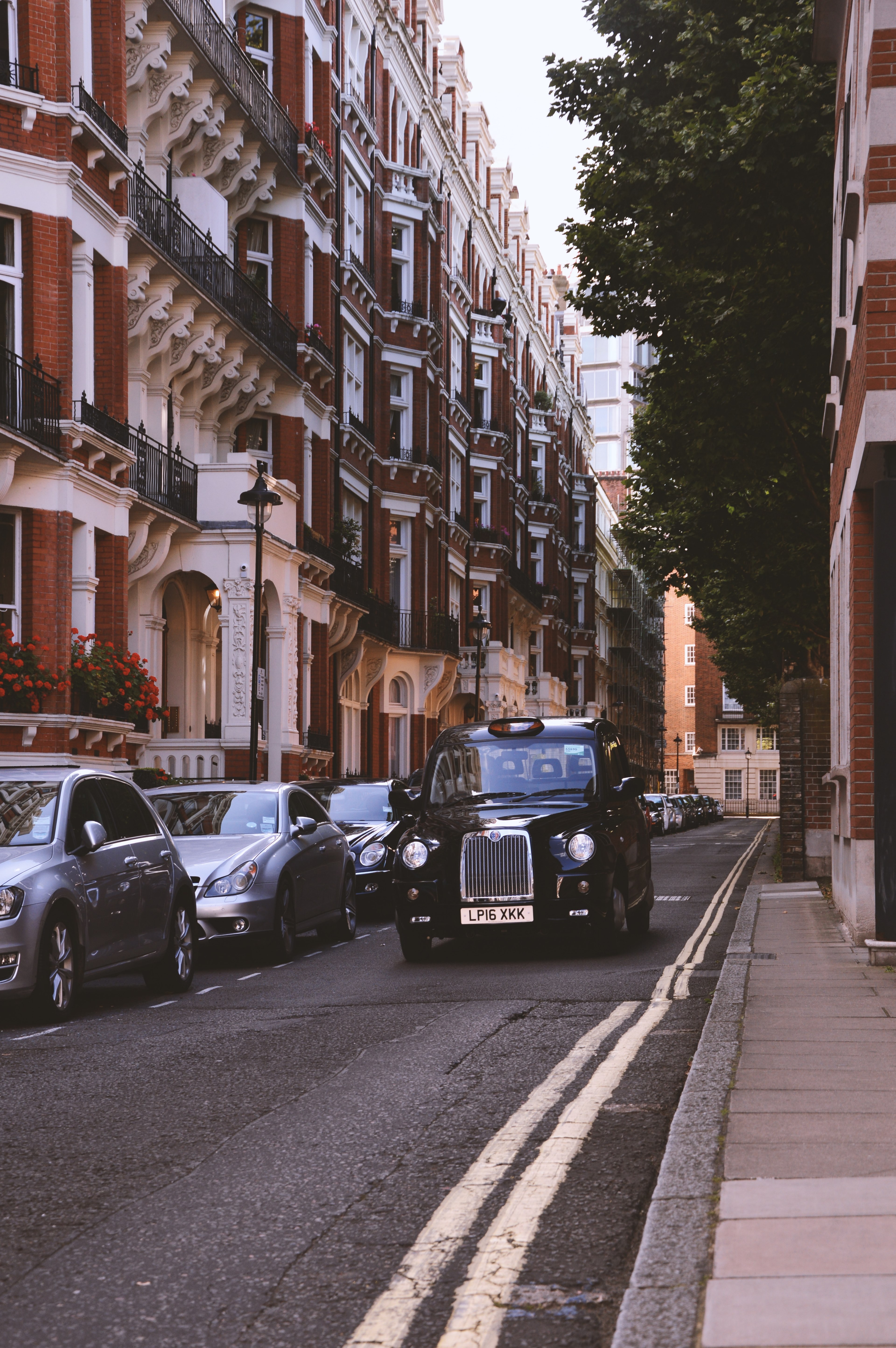 vintage black car driving down a street with brick apartment complexes and other cars along either side, cab in london 4k, Phone HD Wallpaper