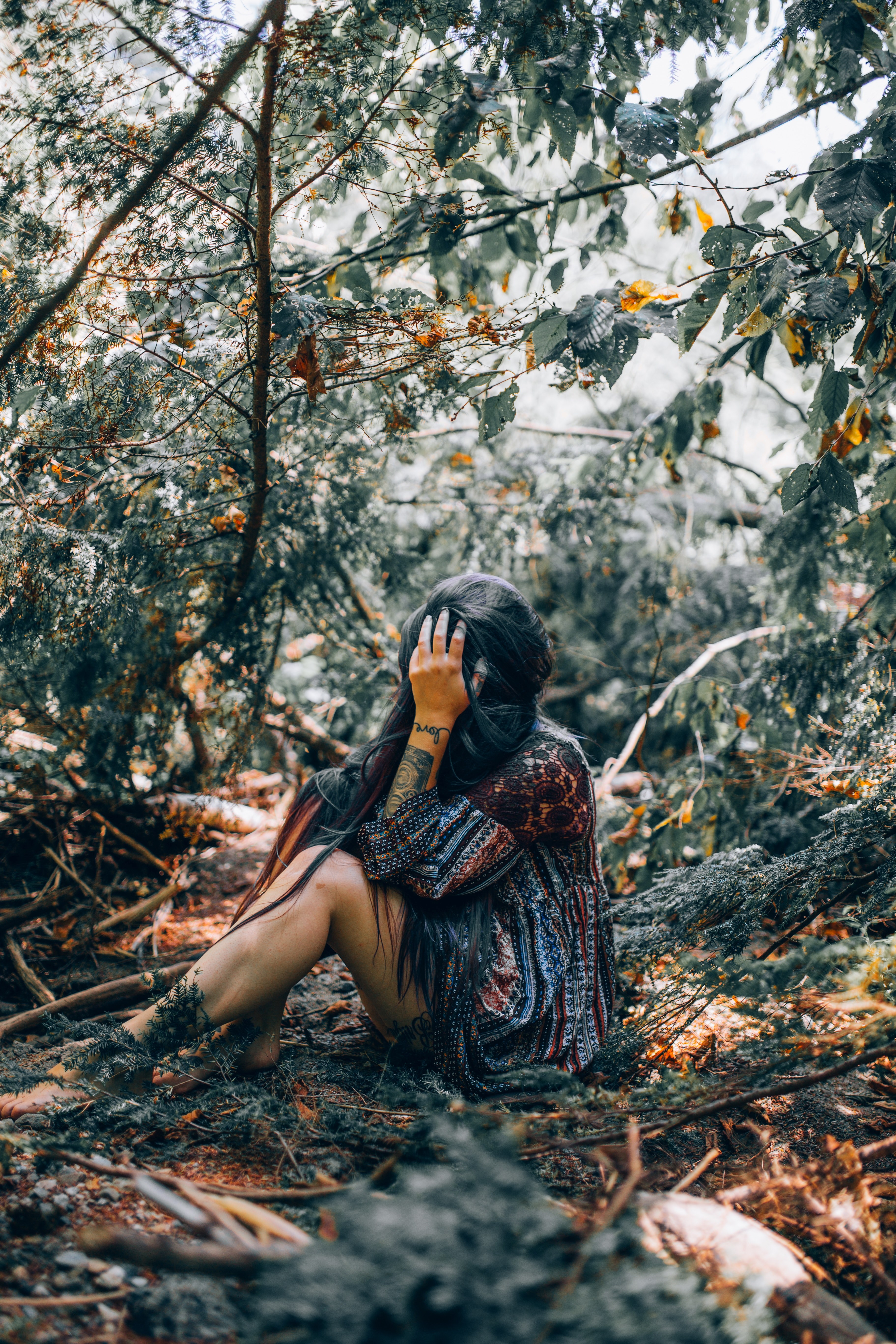 a woman with a forearm tattoo holding her hand over her face while sitting in the woods, _trapped 4k, Phone HD Wallpaper