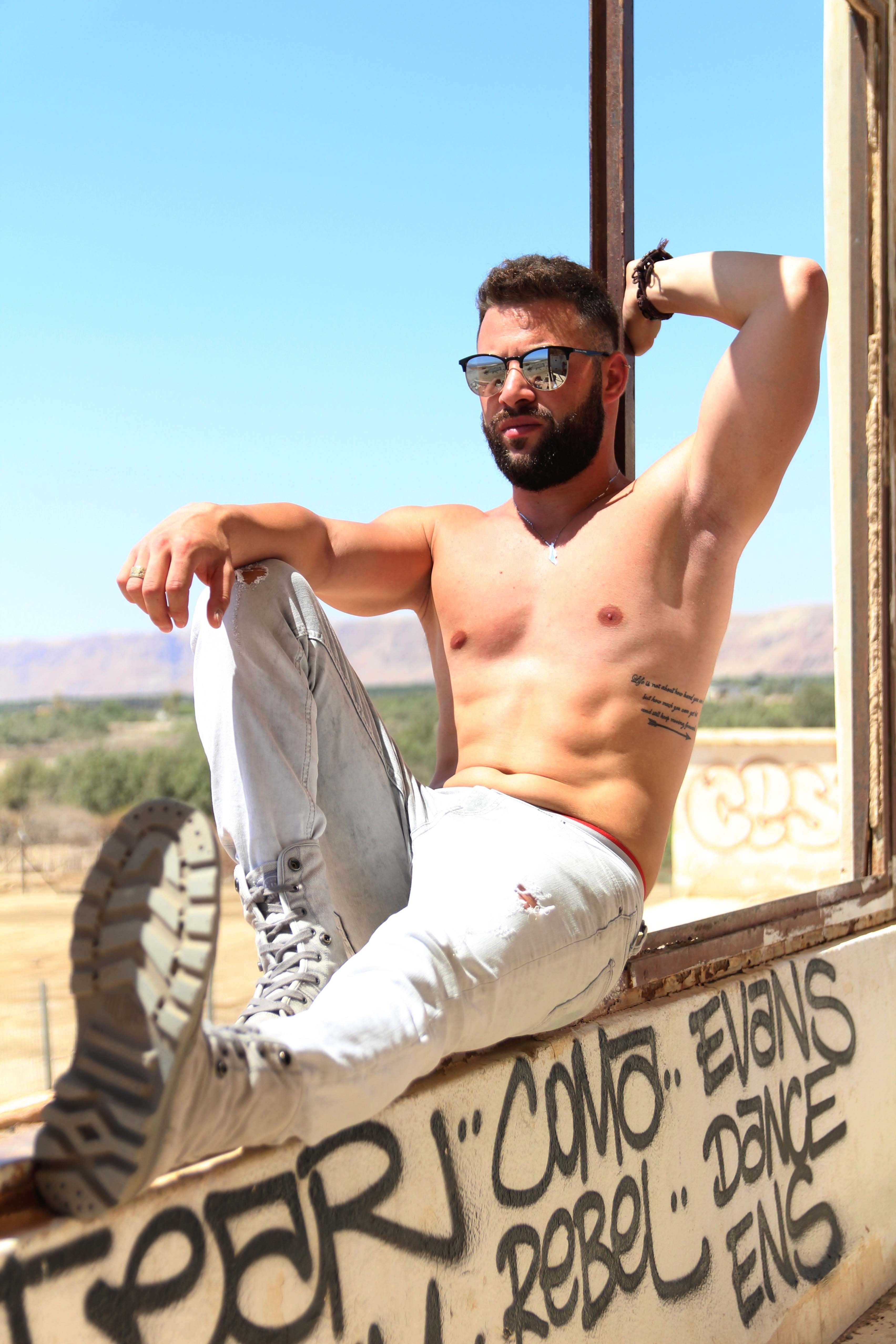 a fit shirtless man poses on a graffitied window frame outdoors by the dead sea, savion moshkevitch 4k, Phone HD Wallpaper
