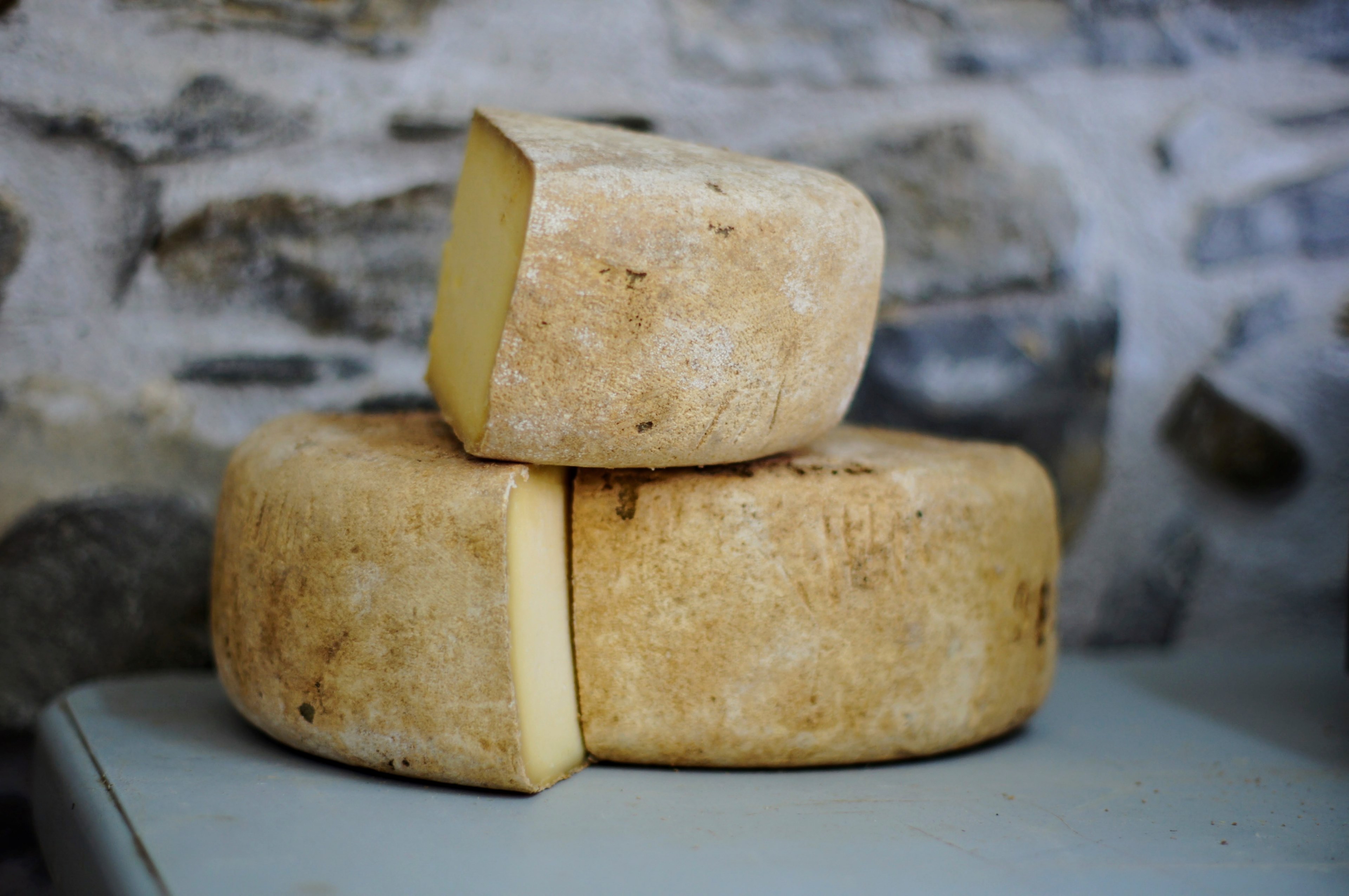 wheel of cheese cut and stacked in front of a stone wall, cut wheels of cheese 4k, HD Wallpaper