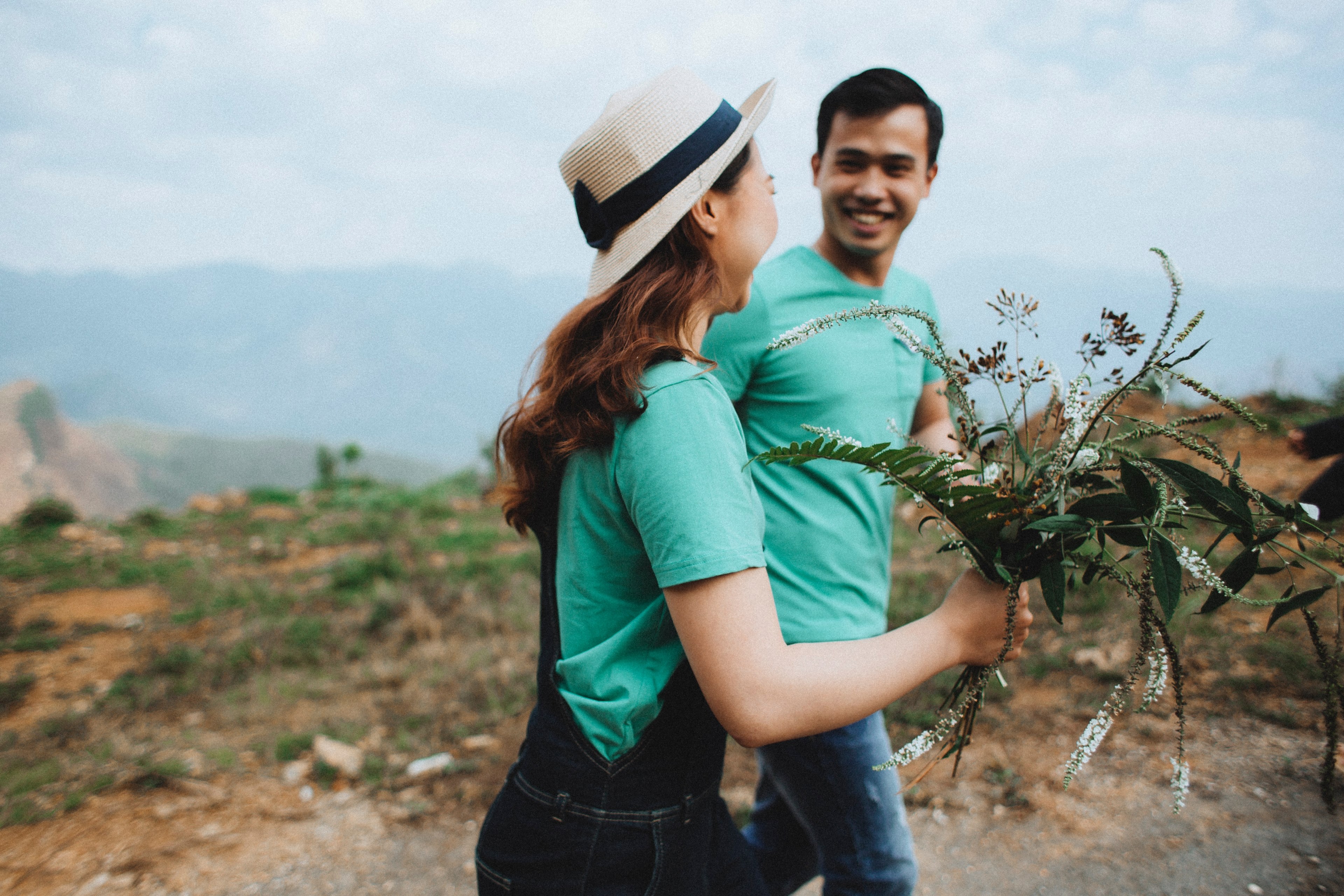 a smiling woman holding a bouquet of flowers walks along a dirt path as a man on her side smiles back at her, happy couple with flowers 4k, HD Wallpaper