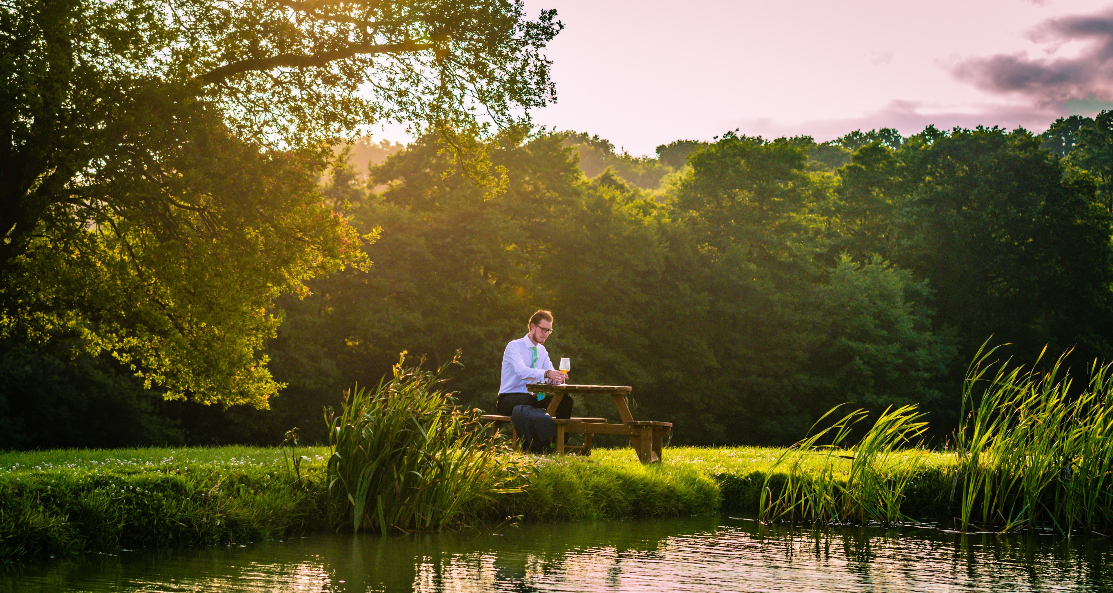 a dressed up man sits alone drinking wine at a picnic table aside a lake and trees, man has picnic alone 4k, HD Wallpaper