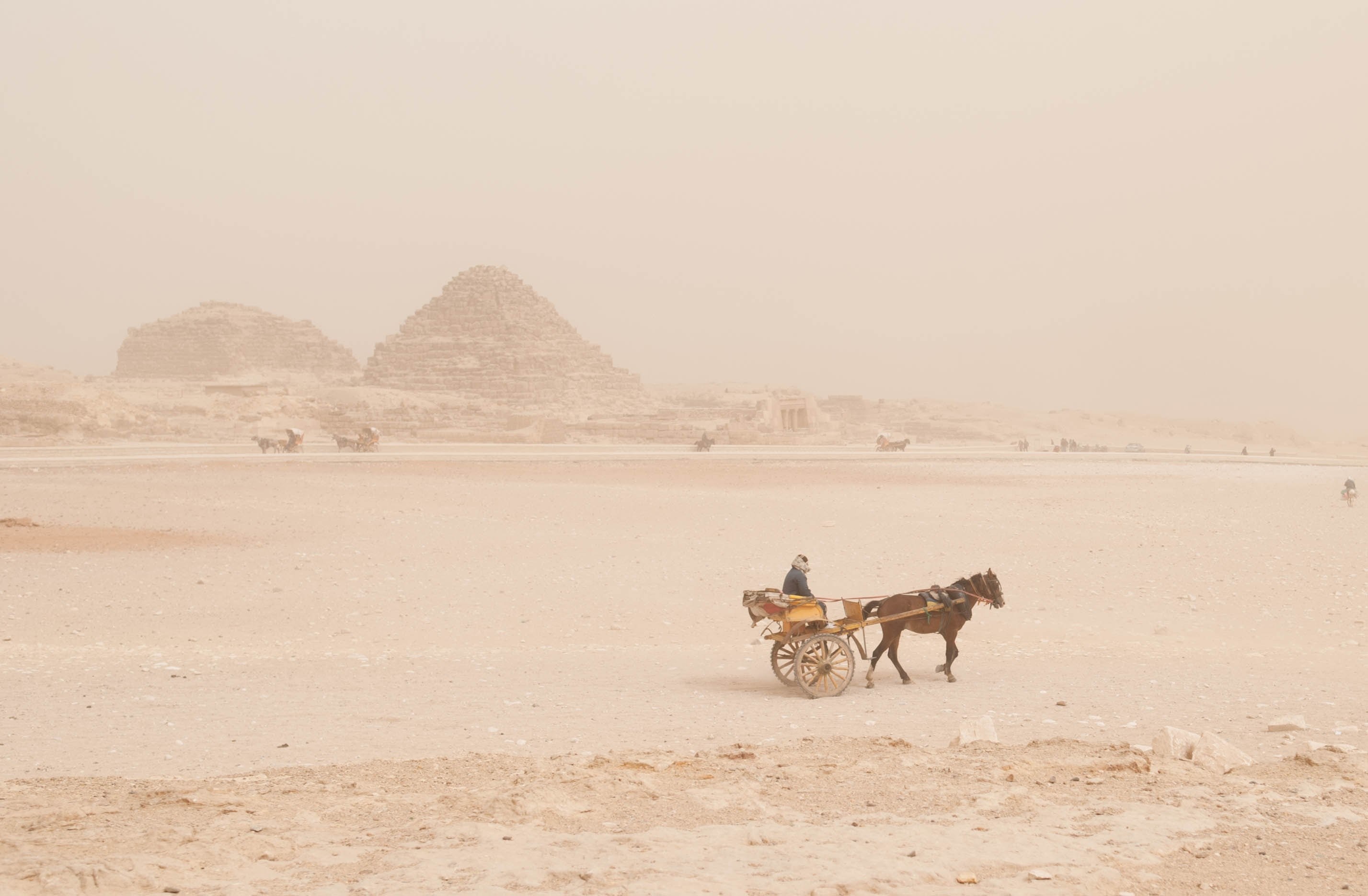 a woman sits on a small cart as a brown horse pulls it through the rocky desert, sandstorm is coming 4k, HD Wallpaper