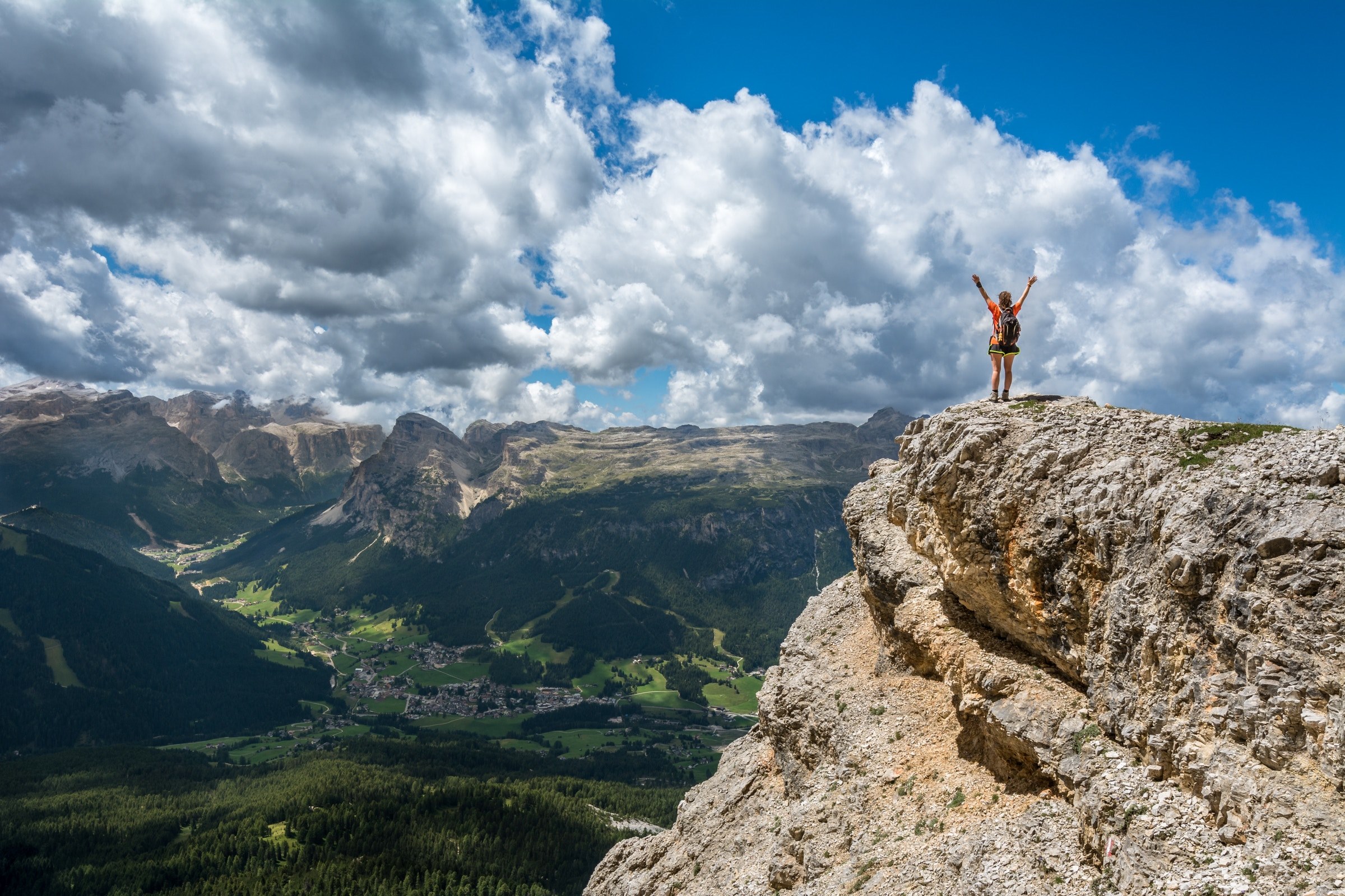 a person throwing their hands up in the air on the edge of a tall jagged rock, looking down to the valley 4k, HD Wallpaper