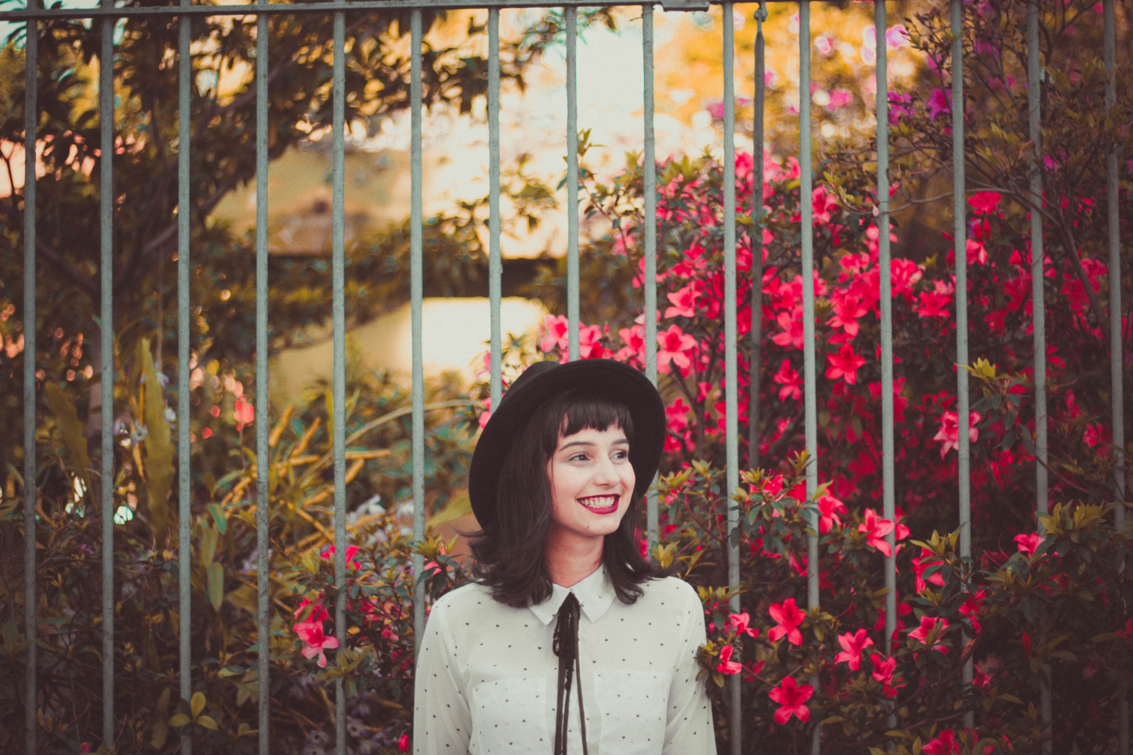 a young woman in a hat smiling while standing next to flower bushes, woman in a hat by red flowers 4k, HD Wallpaper