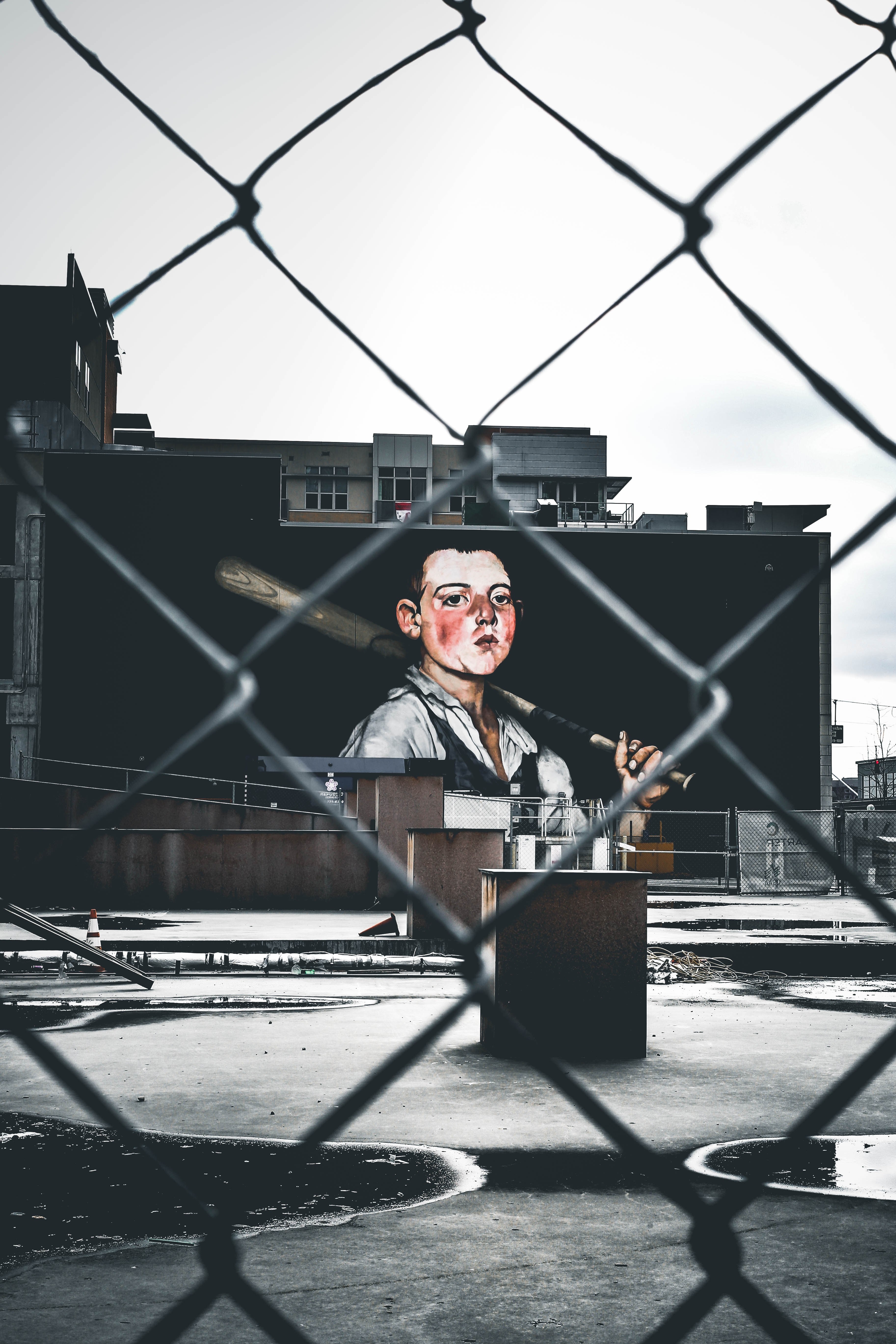 the view of art of man with baseball bat from a chain fence of an urban building, puddles 4k, Phone HD Wallpaper