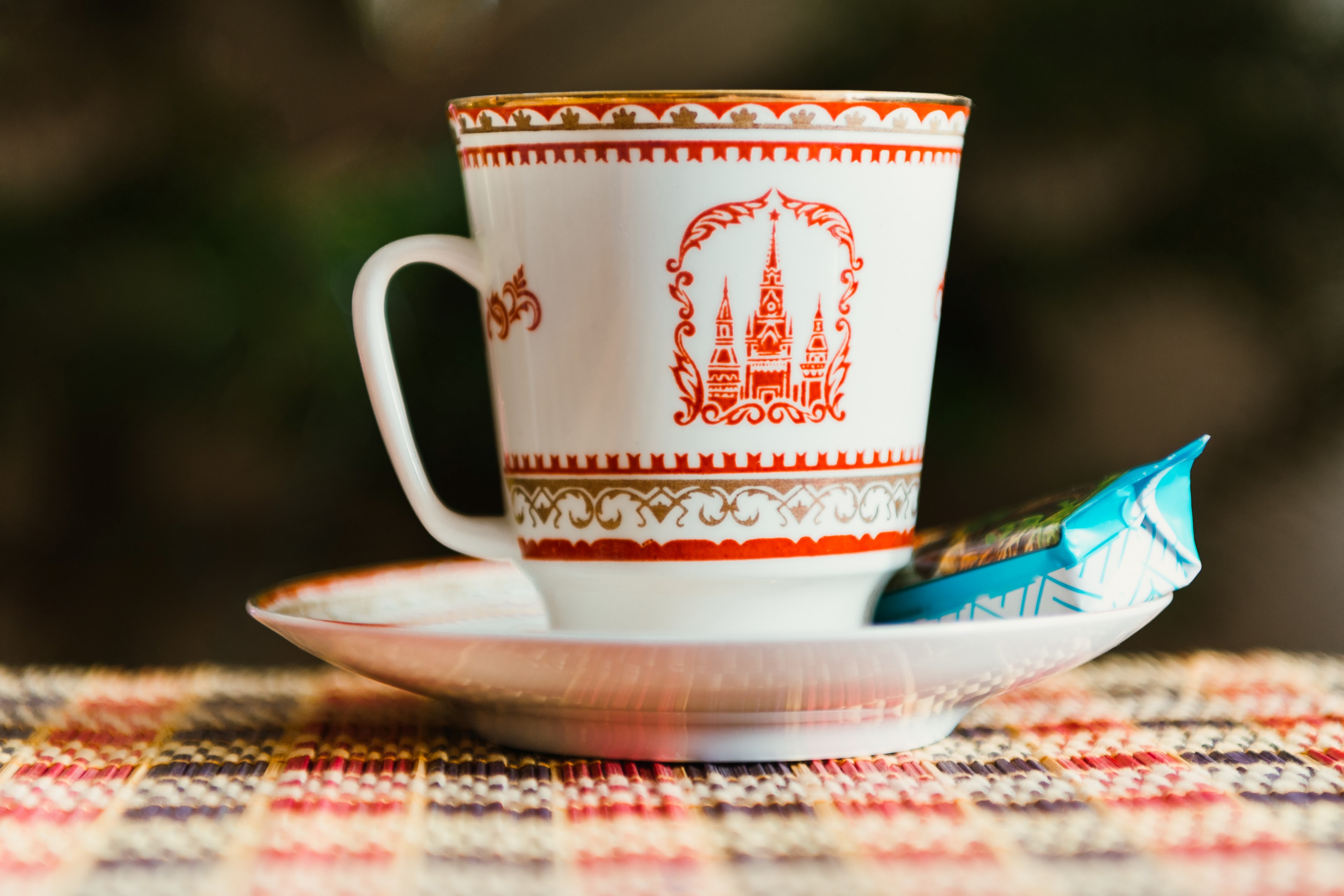 a ceramic cup with a castle on it sitting on a saucer with a biscuit in a wrapper, kremlin cup of tea with candy_ 4k, HD Wallpaper